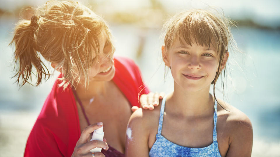Sonnenbrand wegen Corona Mother and daughter on beach. Mother is applying sunscreen lotion on her daughter. The girl is aged 8.