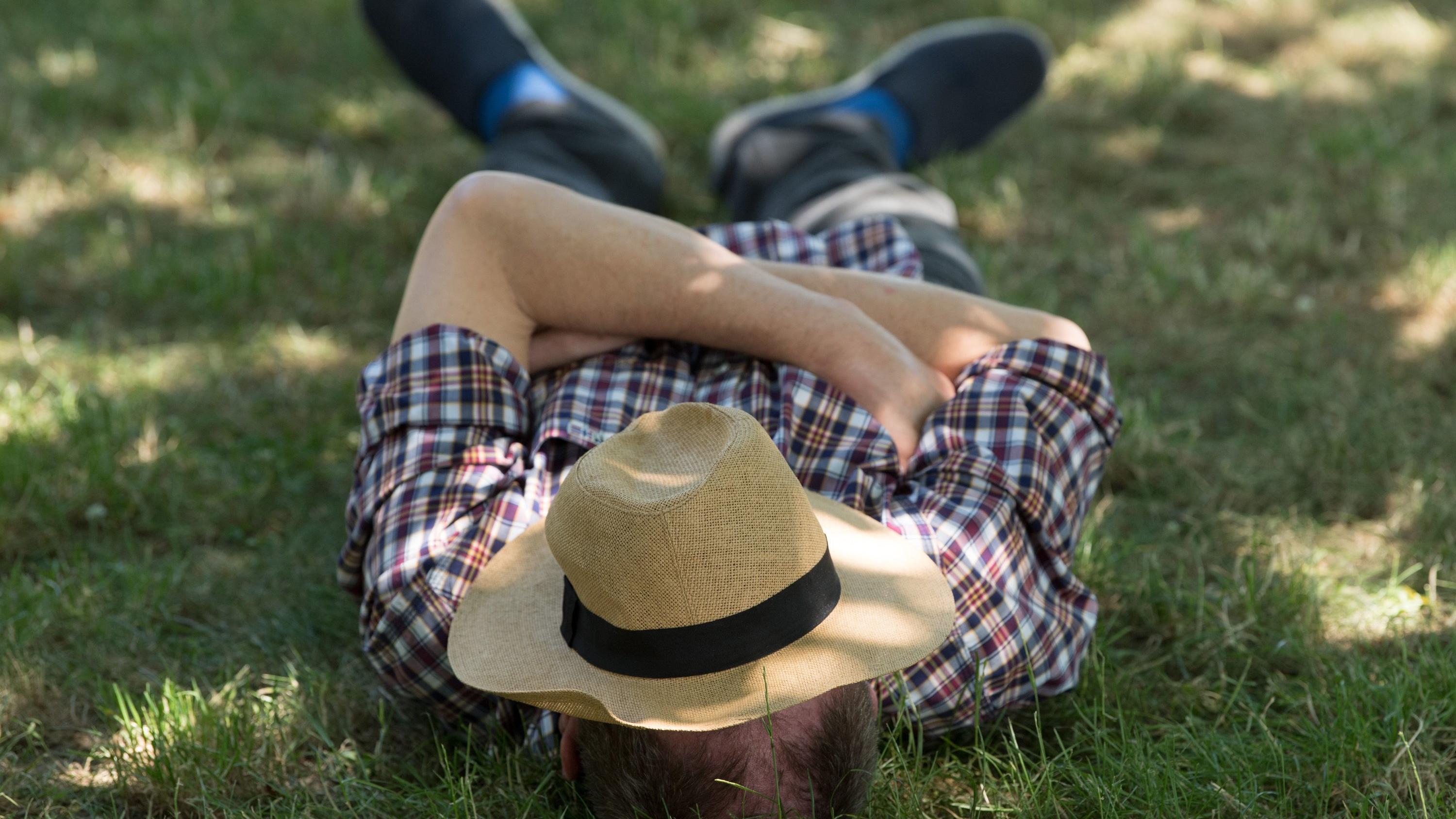 Spanien will sie nicht mehr, in Deutschland wird sie gefordert: Die Siesta! Ein Mann mit einem Sonnenhut auf dem Gesicht liegt auf einer Wiese im Schatten und ruht sich aus. (zu dpa-Korr