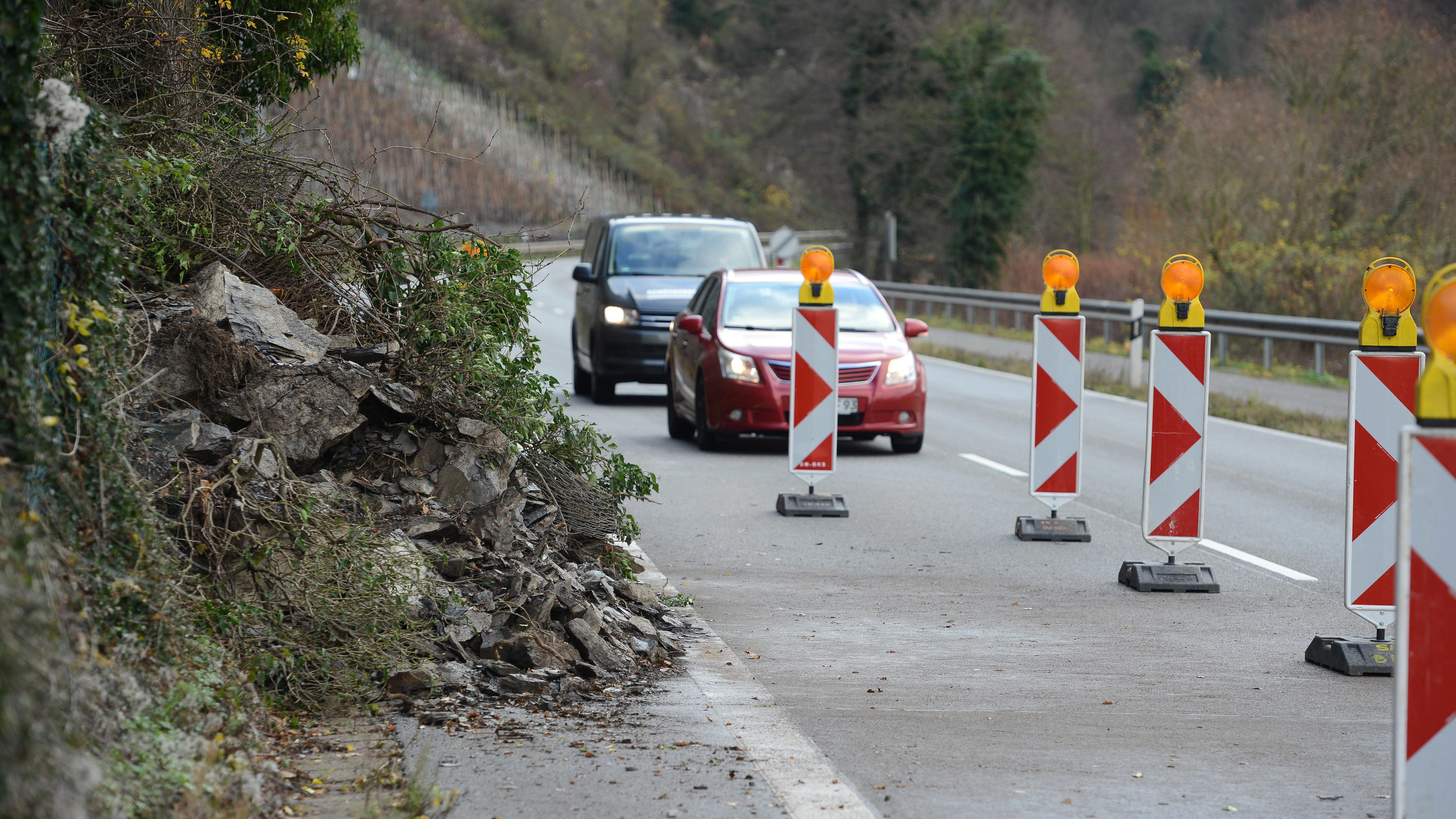 Regensoll ist nach drei Tagen für den Monat schon überschritten! 04.12.2018, Rheinland-Pfalz, Enkirch: Autos fahren auf der Bundesstraße 53 zwischen Enkirch und Traben-Trarbach an einem Felssturz vorbei. Die Straße ist zur Zeit nur einseitig befahrbar. Der starke Regen löste am Montagabend (03.12.2018) rund 30 Ton