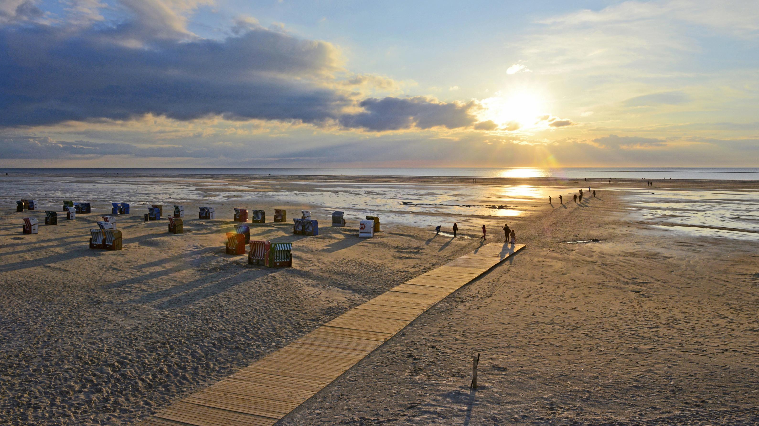 Wetterlexikon: Maritim Maritim: Urlauber als Schattenrisse vor der tiefstehenden Sonne am Strandübergang in Norddorf mit der Nordsee am Horizont
