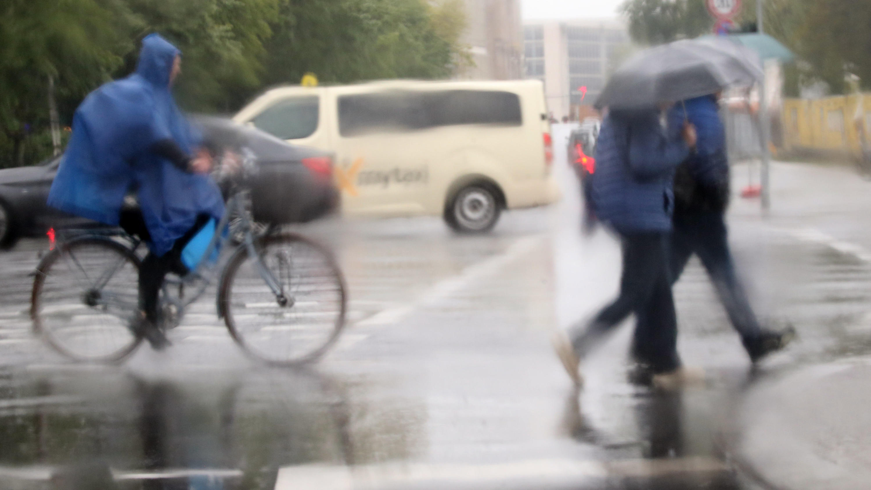 7-Tage-Wetter vom 27.05.2019: Achterbahnfahrt! Absturz und dann kommt der Sommer 16.05.2019, Berlin: Bei Temperaturen um acht Grad Celsius und Regen bewegen sich Passanten und Radfahrer mit Regenschirmen und Regencape durch den Verkehr. Fotografiert durch das Fenster eines Autos.