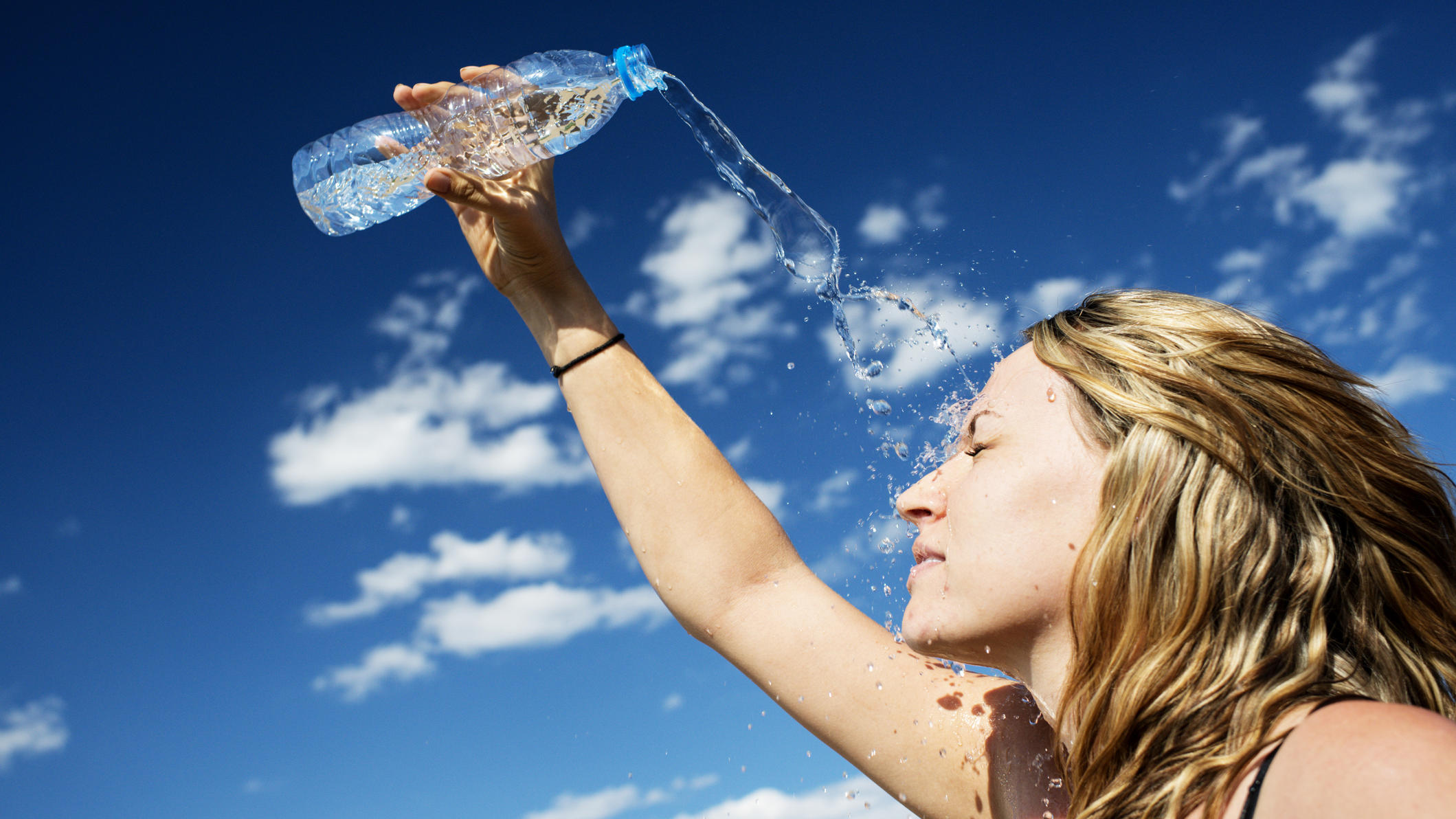 Mit diesen 8 Tipps wappnen Sie sich jetzt gegen heiße Tage Frau schüttet Wasser auf Ihr Gesicht
