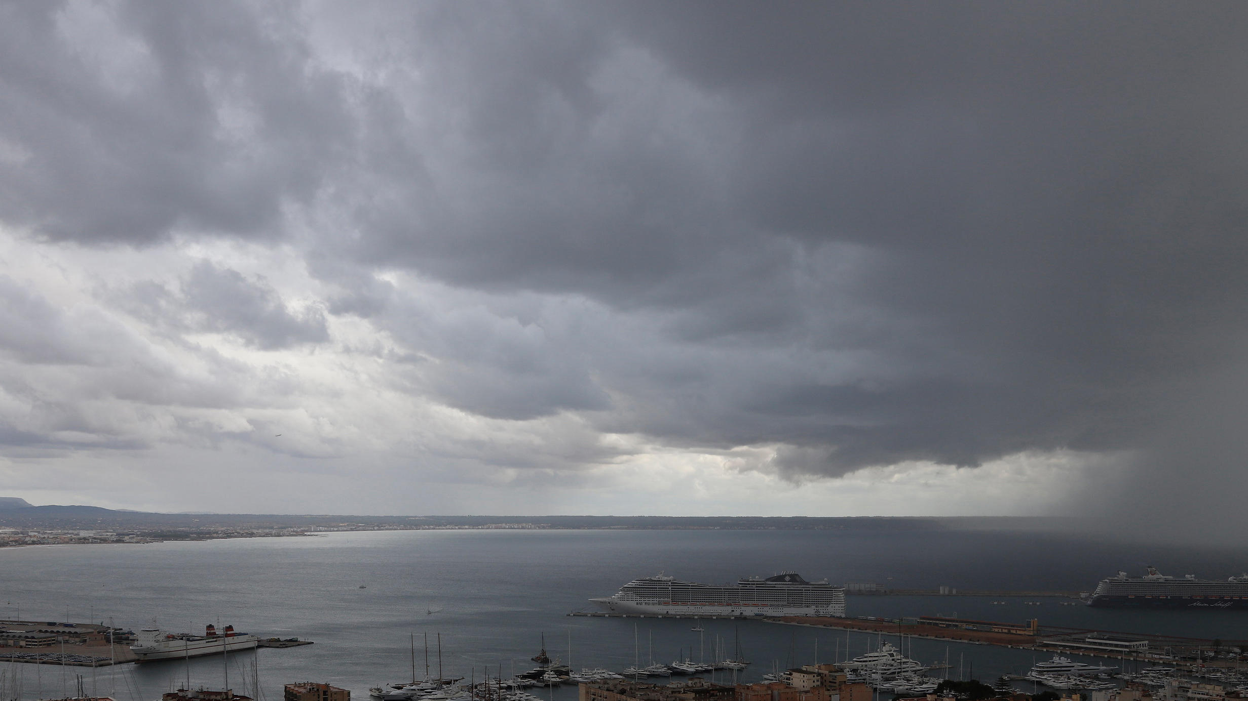 Unwetter auf Mallorca, Ibiza und Menorca: Gewitter, Starkregen, Hagel und Tornados 23.10.2019, Spanien, Palma de Mallorca: Dunkle Regenwolken hängen über der Bucht und dem Hafen, in dem zwei Kreuzfahrtschiffe liegen. Rund ums Mittelmeer haben heftige Unwetter vielerorts Überflutungen und Schäden verursacht. Foto: Clara Margais/dpa