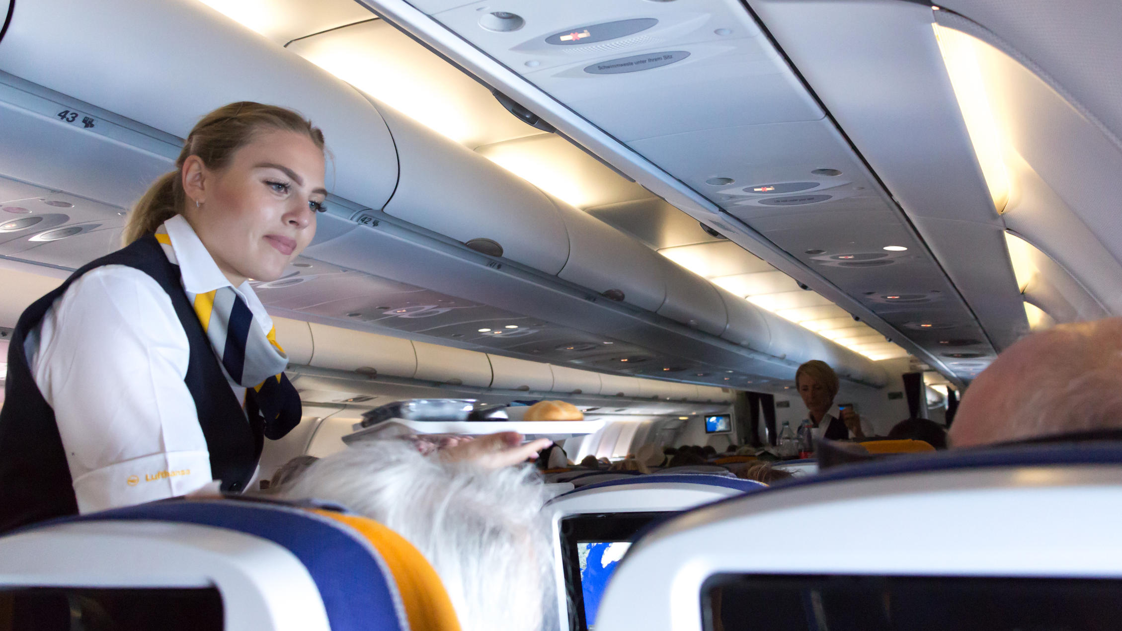 Flugbegleiter wollen Lufthansa zwei volle Tage bestreiken Munich: A female flight attendant is serving the lunch to a passenger sitting in the economy class of the route Munich - Vancouver of Lufthansa Airlines.