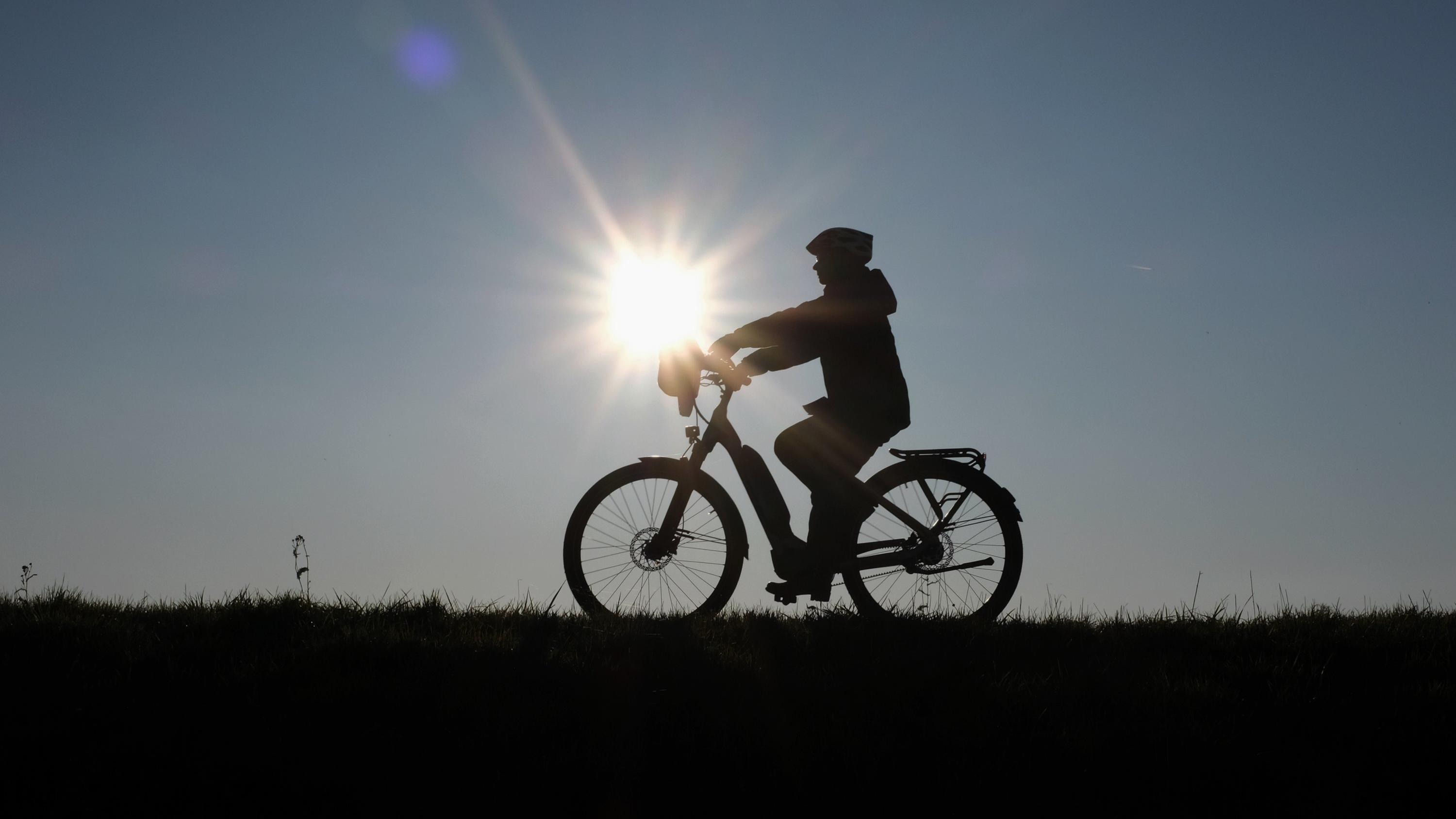 Die RTL Winter-Wetter-Garantie zum vierten Advent Eine Frau fährt bei untergehender Sonne mit ihrem Fahrrad über den Deich am Rhein. Foto: Martin Gerten/dpa +++ dpa-Bildfunk +++