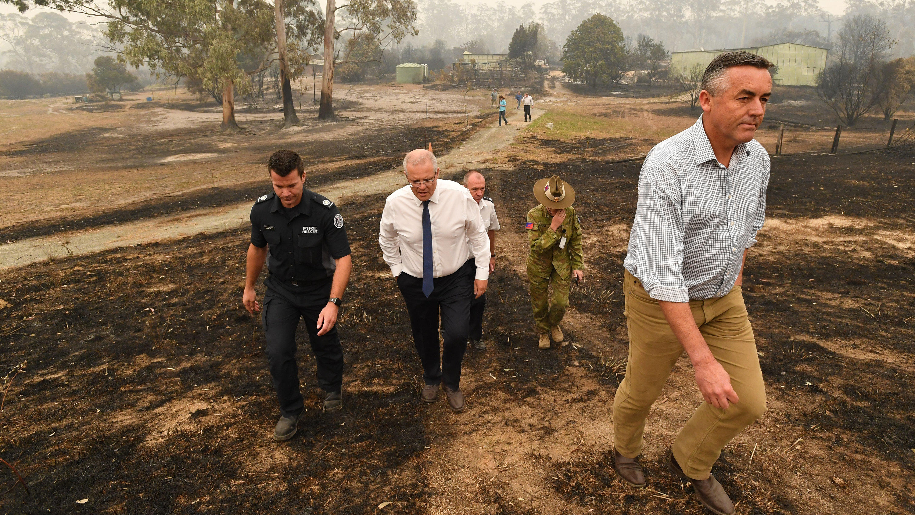 Ist der Klimawandel schuld an den Buschfeuern in Australien? 03.01.2020, Australien, Bairnsdale: Scott Morrison (M), Premierminister von Australien, und Darren Chester (r), Mitglied des Repräsentantenhauses von Gippsland, besichtigen die vom Feuer verwüsteten Wildflower-Farm von Paul und Melissa Churchman in S
