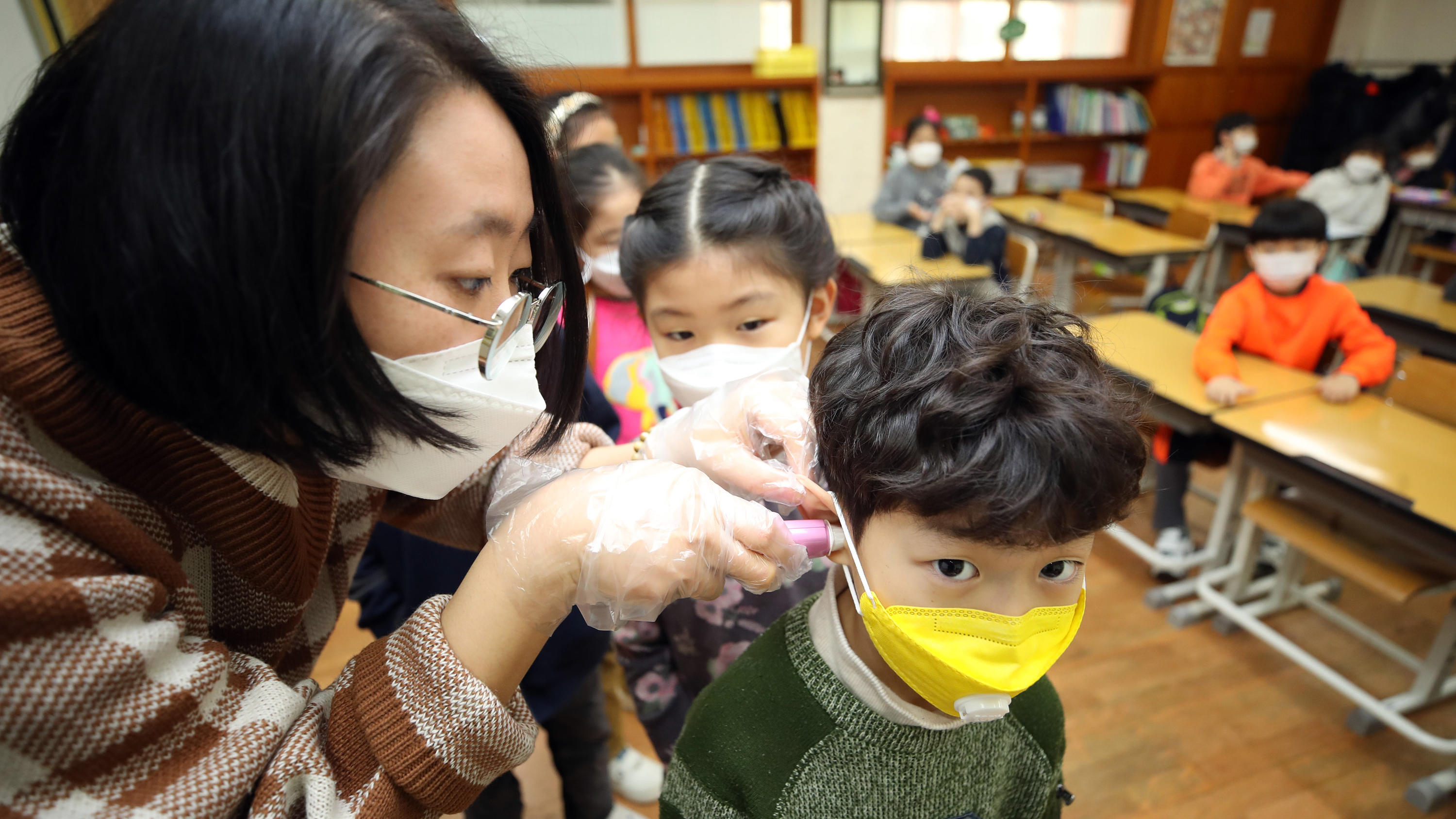 Coronavirus-Chronik Teil 1 30.01.2020, Südkorea, Seoul: Eine Lehrerin misst am ersten Schultag nach den Winterferien die Temperaturen eines Grundschülers. Die Zahl der Infektionen und Todesopfer durch die Lungenkrankheit aus China ist erneut gestiegen. Foto: -/YNA/dpa +++ dpa-
