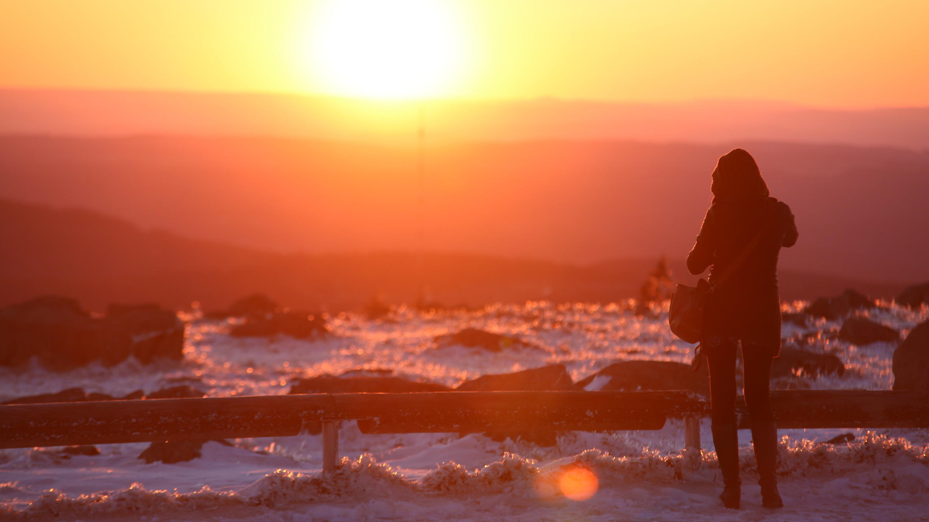 7-Tage-Wettertrend: Kalte Zeiten mit viel Sonnenschein 22.03.2020, Sachsen-Anhalt, Schierke: Eine Frau steht auf dem Brocken und fotografiert die Harzberge im Licht der untergehenden Sonne. Foto: Matthias Bein/dpa-Zentralbild/dpa +++ dpa-Bildfunk +++