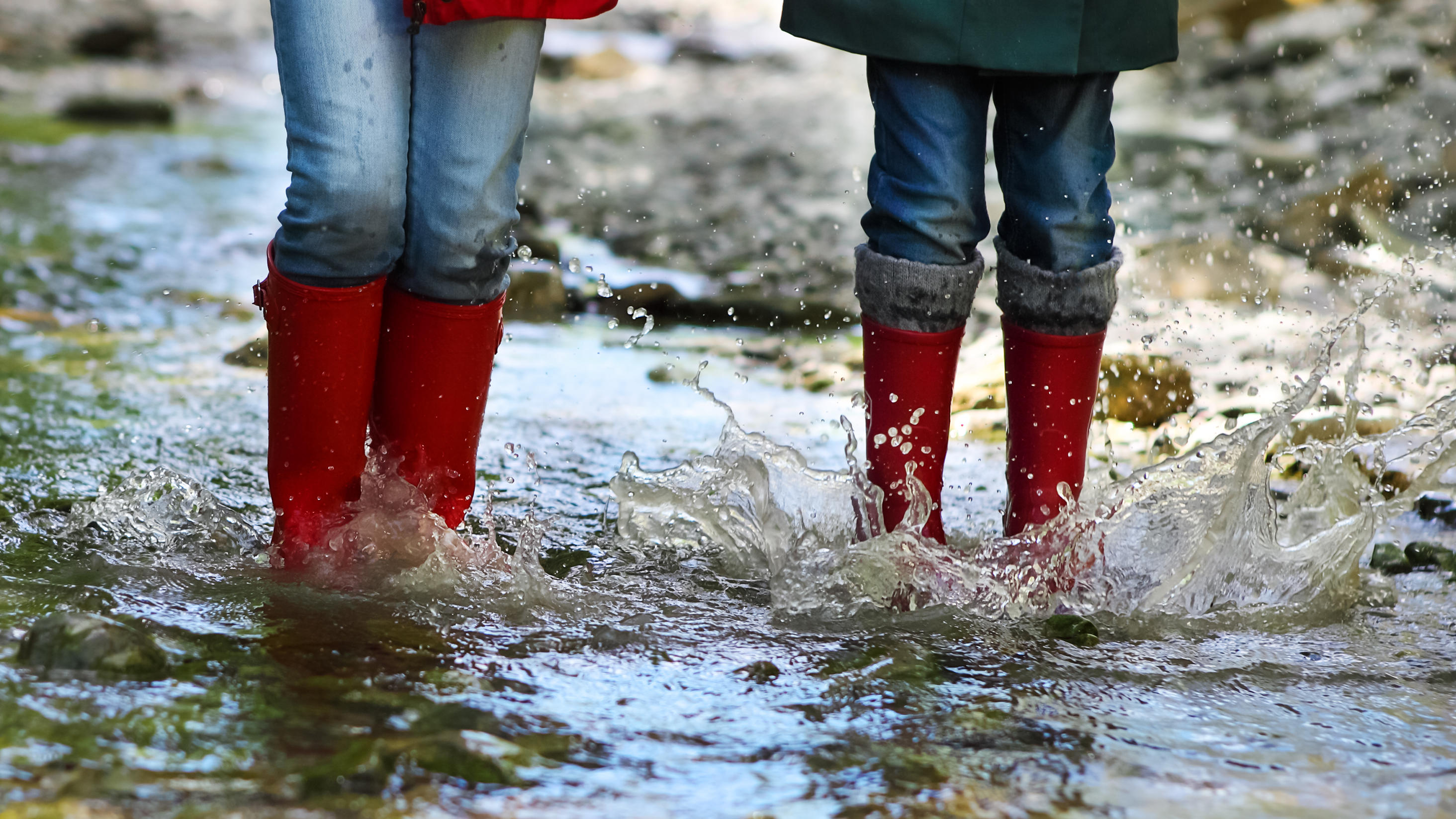 1. Mai 2020: Vorsicht, Wetterumschwung! Gewitter, Wind und viel Regen Children wearing rain boots jumping into a mountain river. Close up