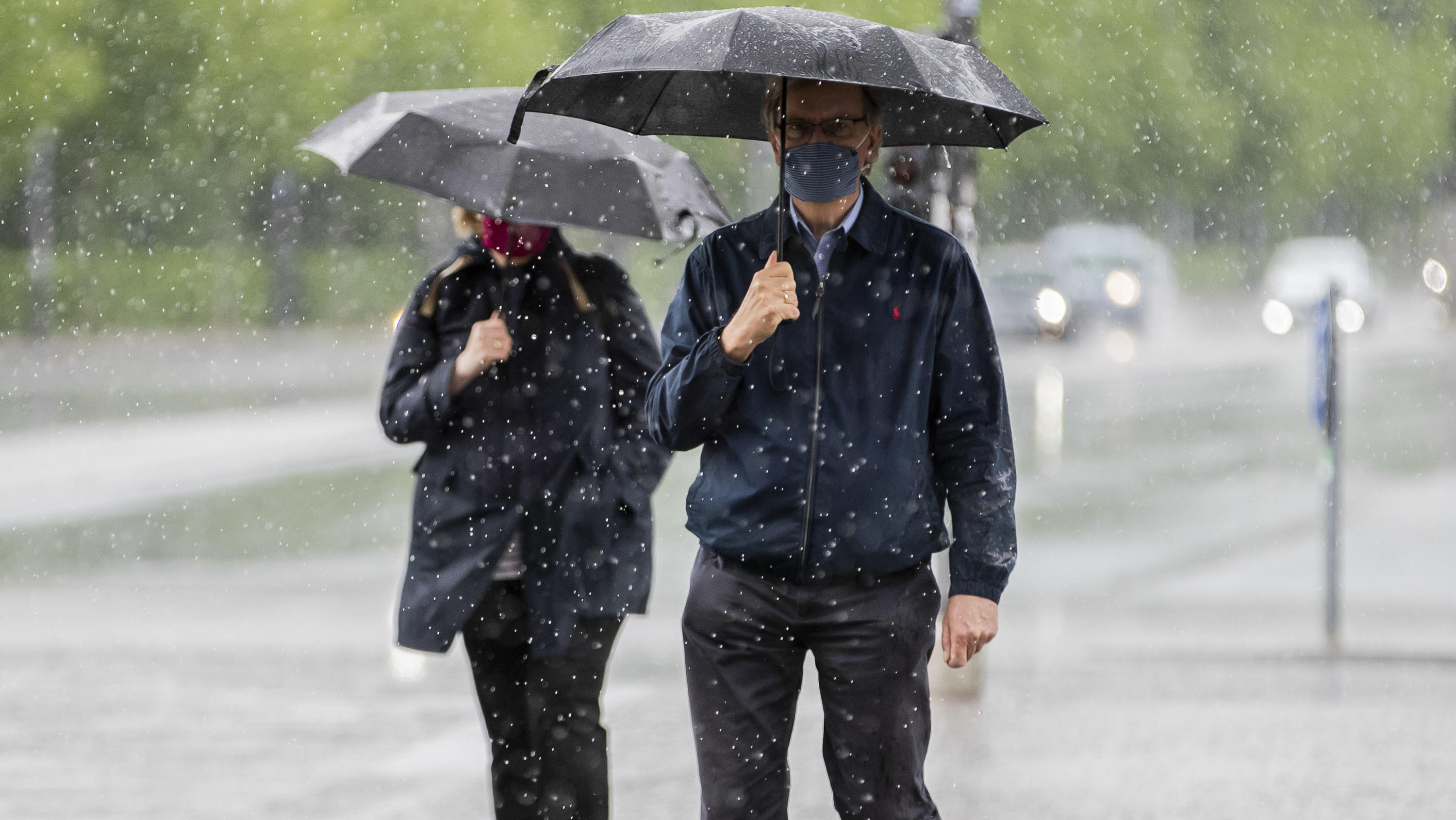 Wettertrend für 7 Tage: Schafskälte und immer wieder nass 02.05.2020, Berlin: Ein Mann und eine Frau gehen bei starkem Regen mit Mund-Nasen-Schutz und Regenschirmen über den Platz des 18. März. Foto: Christoph Soeder/dpa +++ dpa-Bildfunk +++