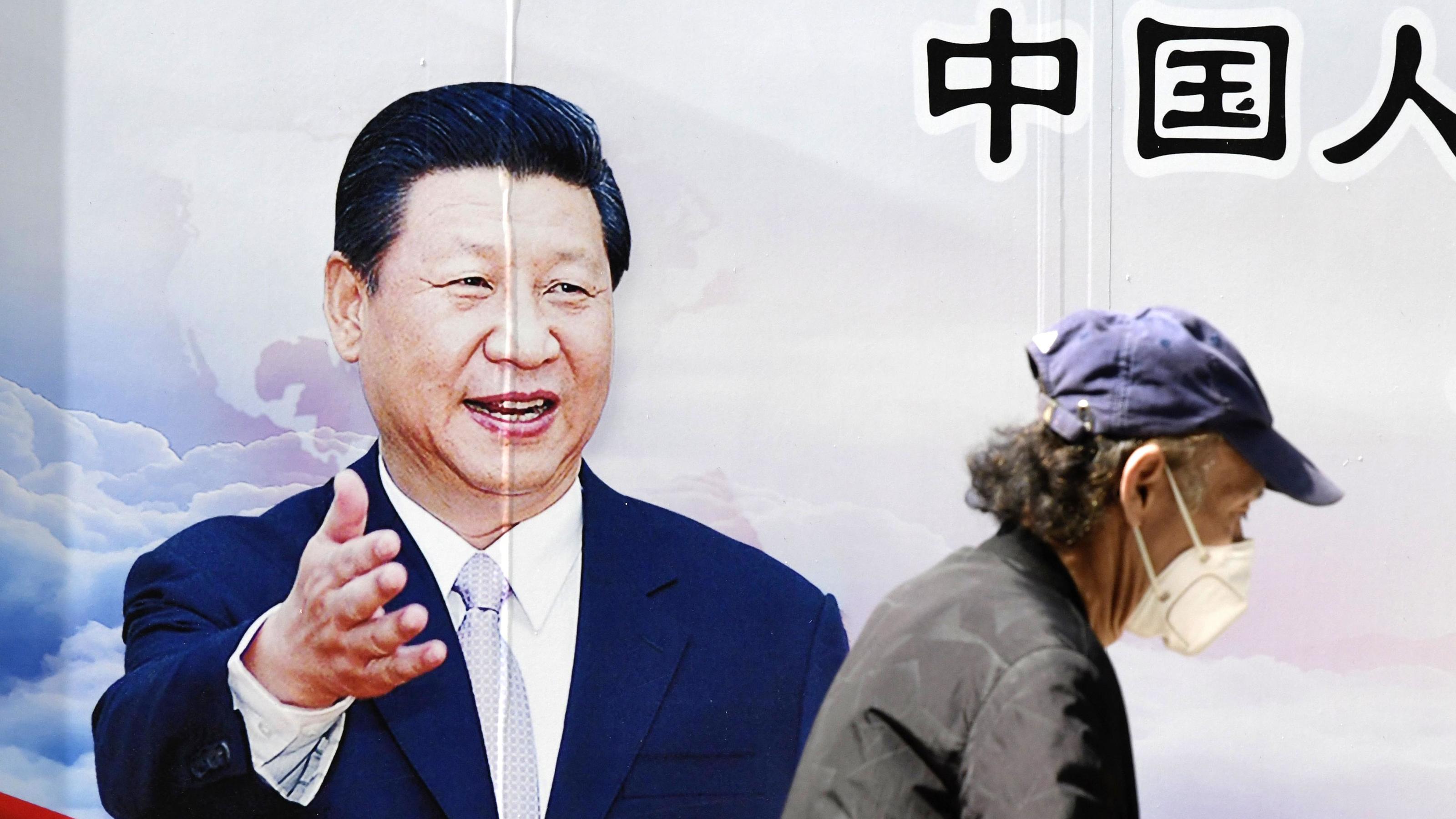Verschweigt China eine zweite Corona-Welle? Ein Mann spaziert mit einer Maske an einem Plakat von Chinas Präsident Xinping vorbei. Foto: -/kyodo/dpa +++ dpa-Bildfunk +++