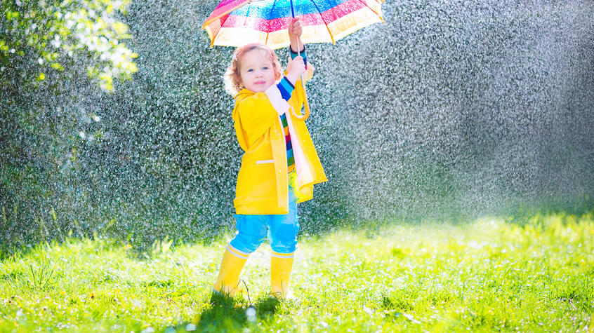 Top-Regenjacken für Kids: Spaß bei jedem Wetter Funny cute curly toddler girl wearing yellow waterproof coat and boots holding colorful umbrella playing in the garden by rain and sun weather on a warm autumn or sumemr day