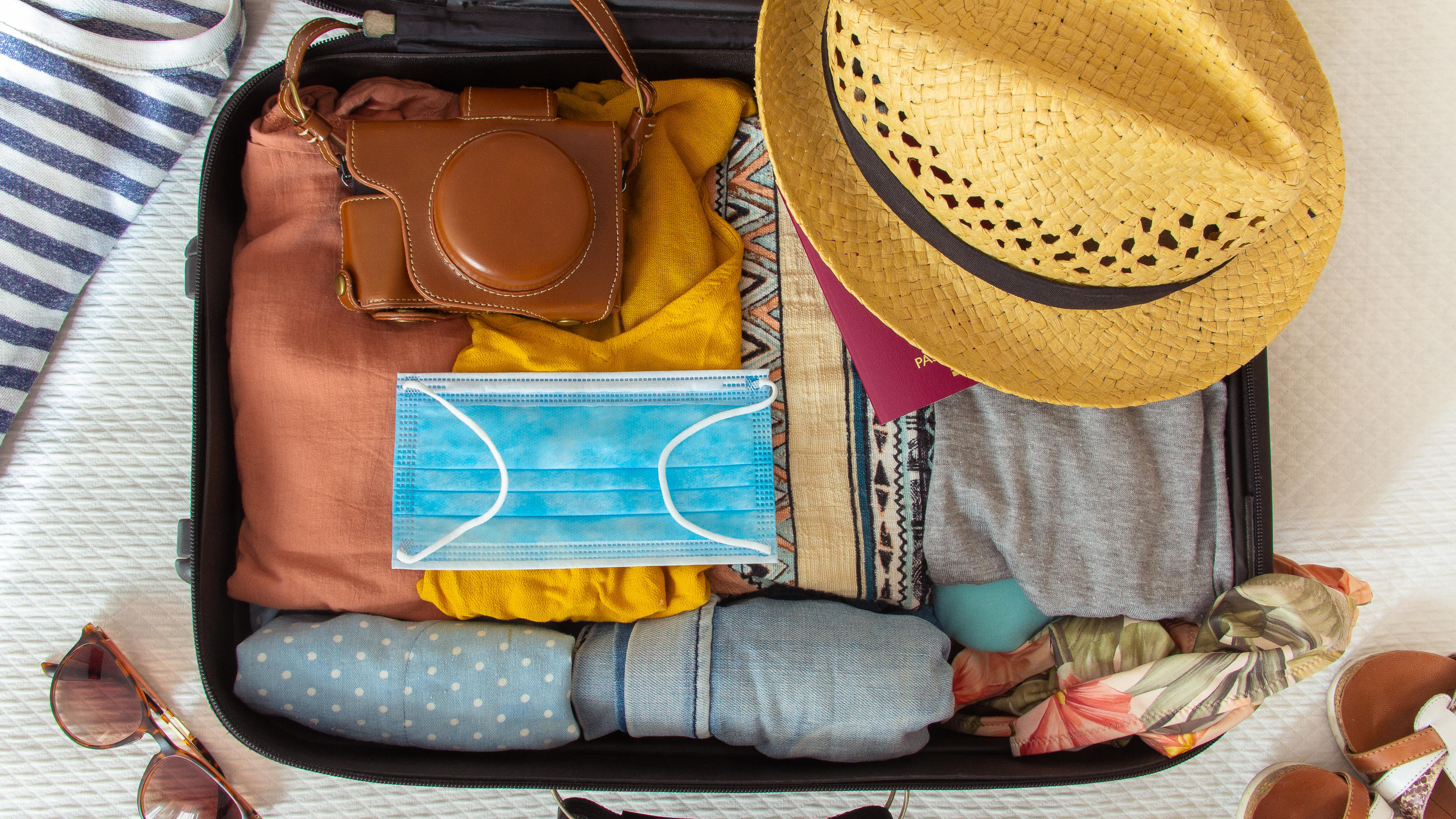 Aus diesen Urlaubsländern reist das Virus ein Suitcase prepared to travel in summer, in the new normal, after the coronavirus covid 19 pandemic, with a face mask among the luggage. There are other accessories like a hat, sunglasses, camera. Concept of quarantine, coronavirus, summer vacation in