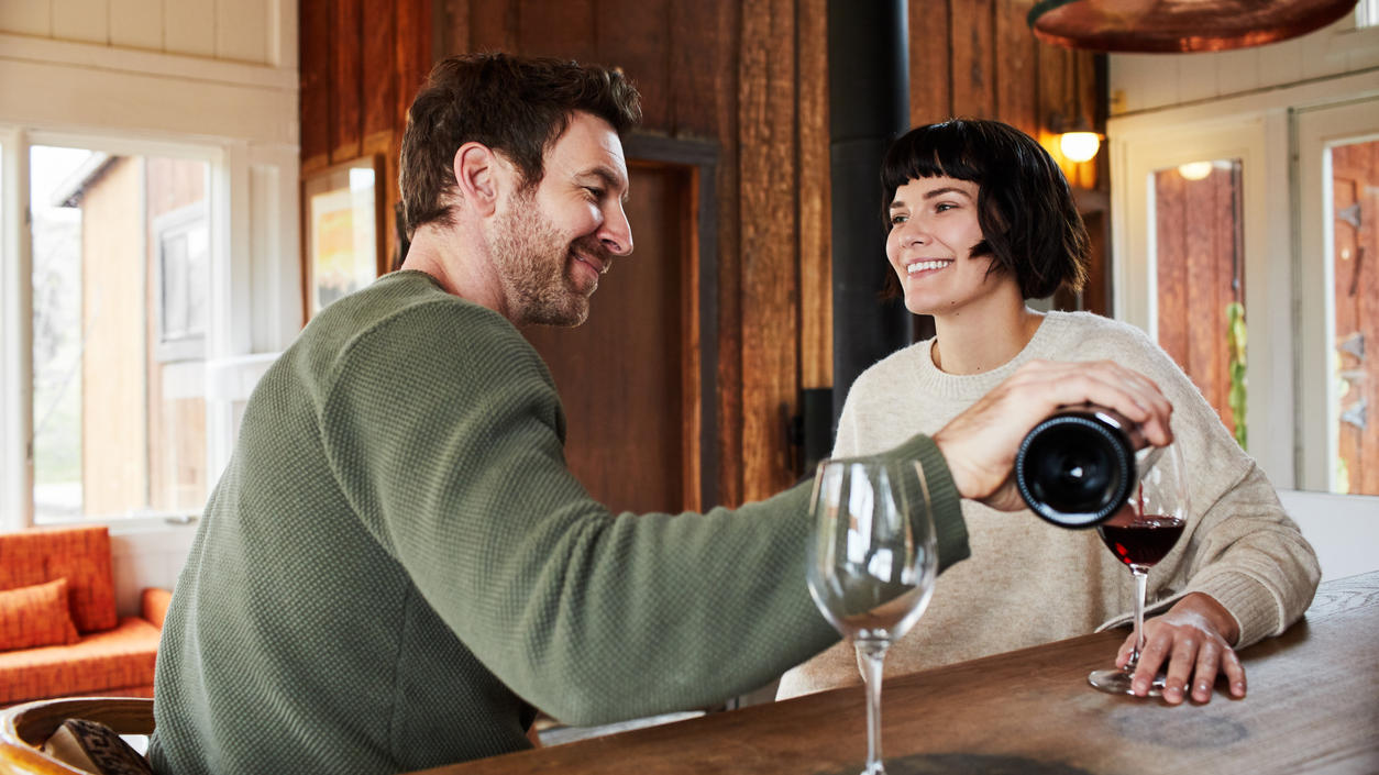 Warum haben Wein- und Sektflaschen einen gewölbten Boden? Mann schenkt Frau ein Glas Rotwein ein
