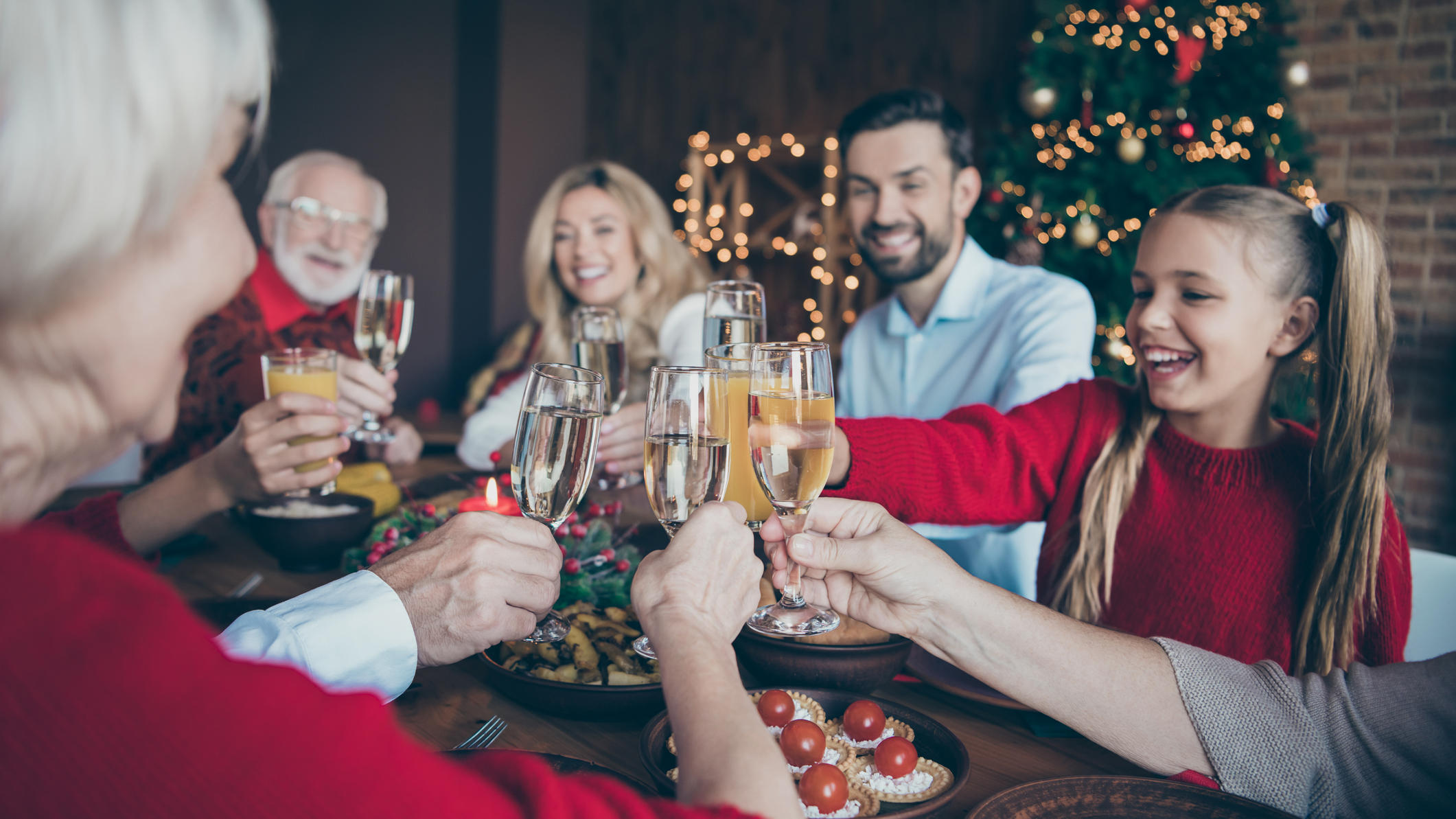 Darf ich an Weihnachten meine Familie besuchen? Familie stößt unterm Weihnachtsbaum an.
