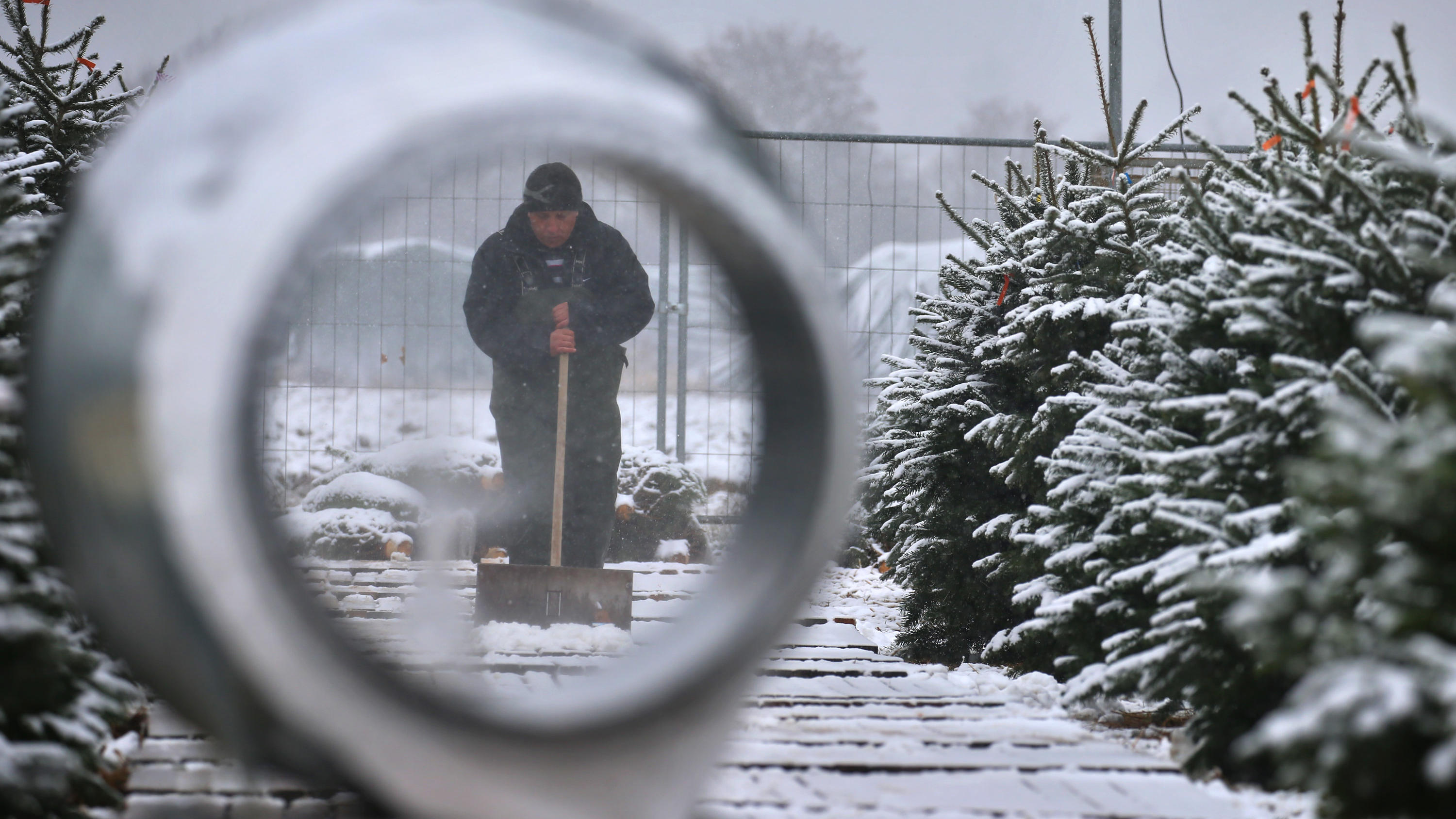 Darum kommen uns die nächsten Tage so kalt vor Ein Christbaumverkäufer räumt zwischen seinen Bäumen Schnee.