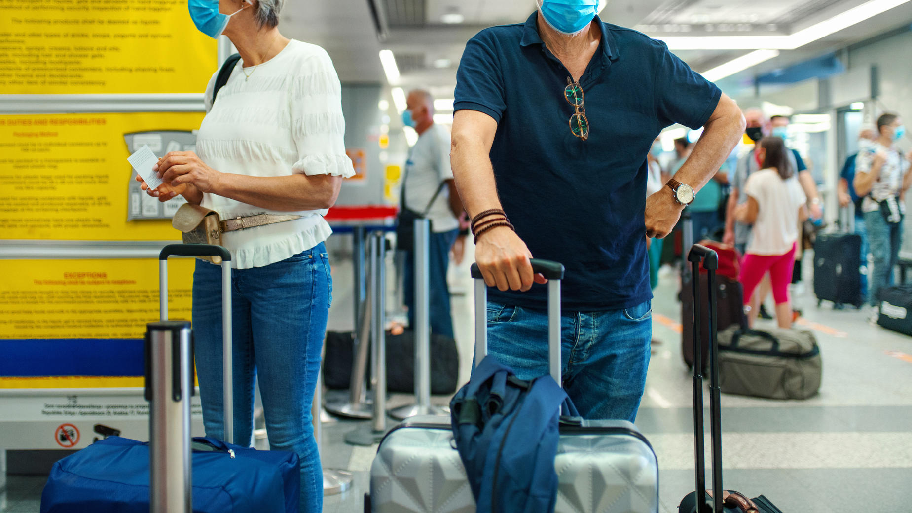RKI stuft mehr als 20 Länder als Hochrisikogebiete ein Mann und Frau mit Corona-Masken am Flughafen