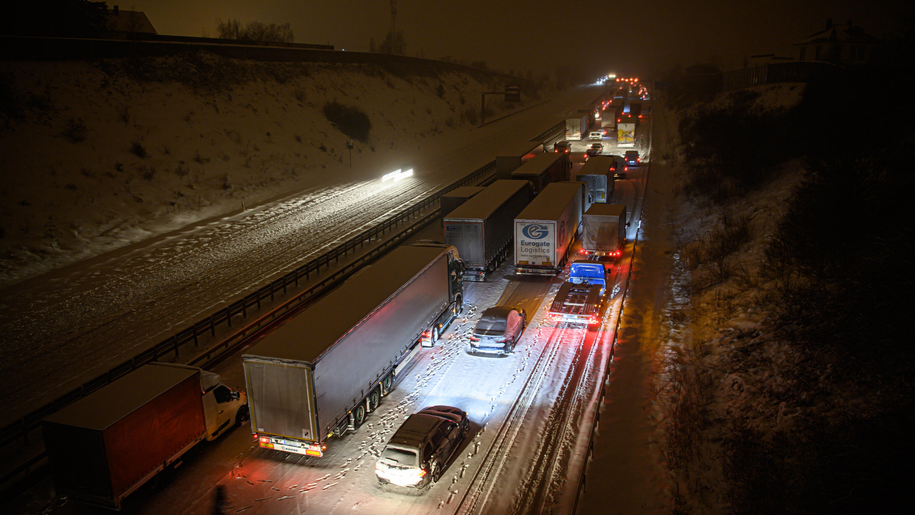 Zwei Tote im Schnee entdeckt ++++ Dach von Holzfachhandel eingestürzt 08.02.2021, Sachsen, Dresden: Autos und Lastwagen stehen am frühen Morgen bei Schneefall auf der verschneiten Autobahn 4 bei Dresden im Stau, während ein Mann neben seinem Auto steht. Foto: Robert Michael/dpa-Zentralbild/dpa +++ dpa-Bildfunk +++