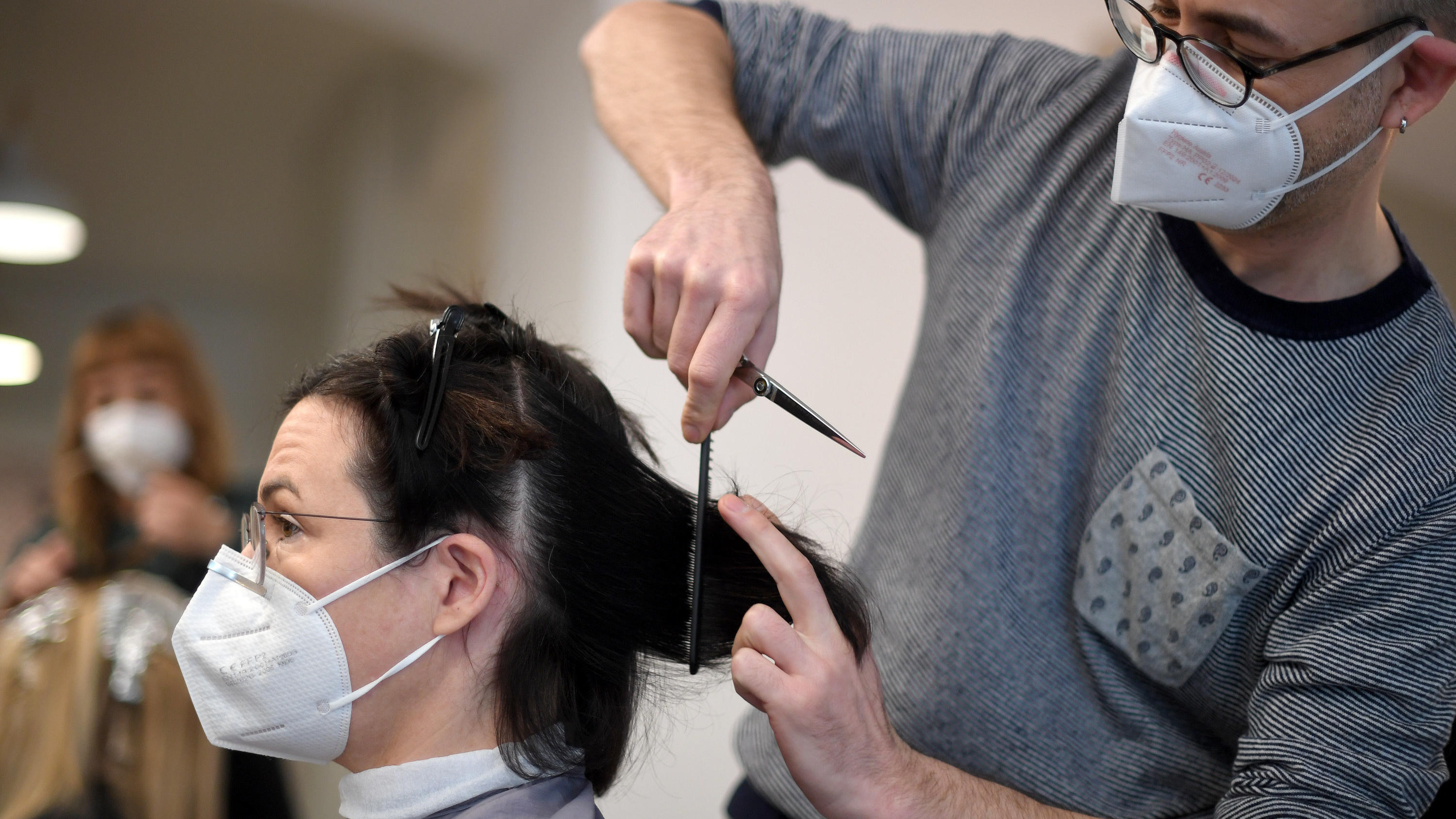Die wichtigsten Änderungen zum März 2021 Ein Friseur schneidet einer Kundin in seinem Salon die Haare; beide tragen FFP2-Masken.