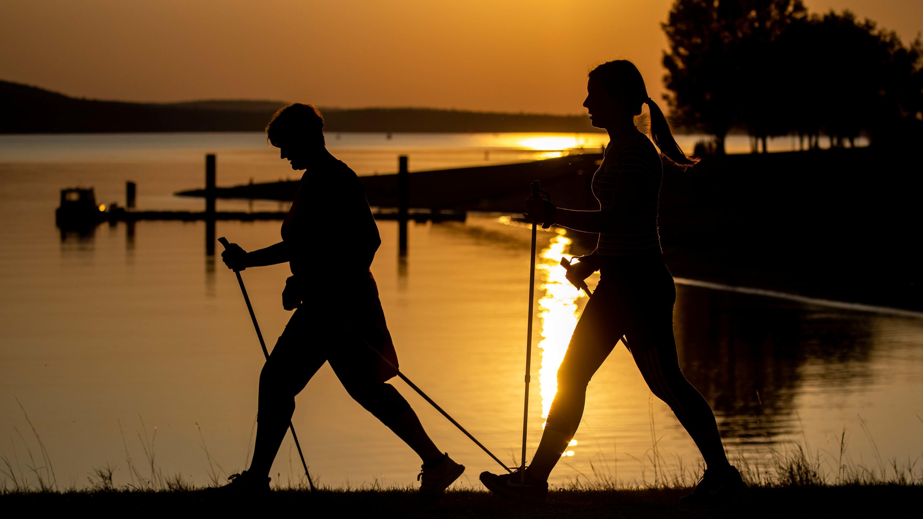 Nordic Walking: So sind Sie optimal ausgerüstet für das Training 21.09.2020, Bayern, Allmannsdorf: Zwei Frauen gehen in der Abendsonne auf dem Damm des Brombachsees mit Nordic Walking-Stöcken. Foto: Daniel Karmann/dpa +++ dpa-Bildfunk +++