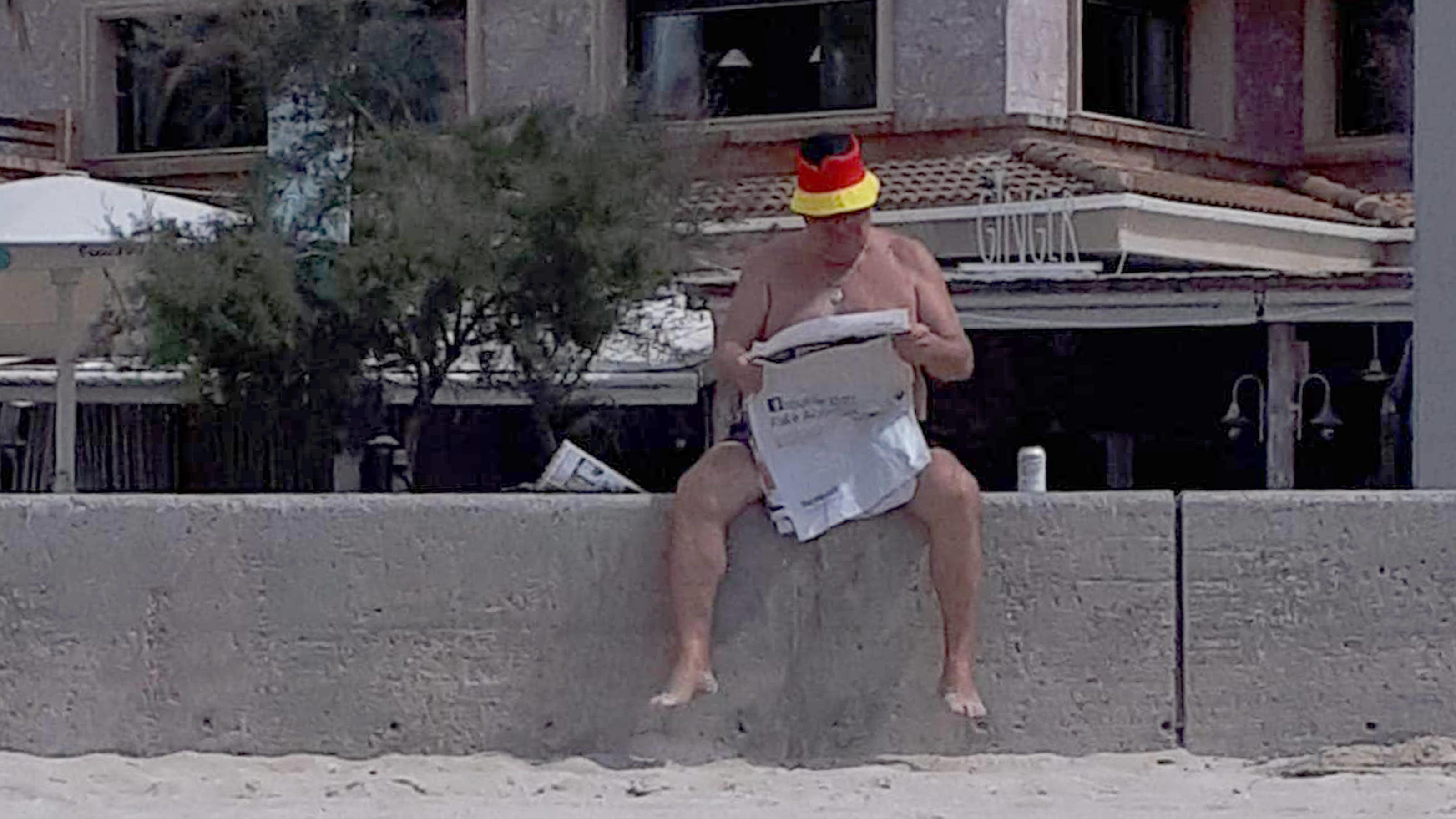 Mallorca-Urlaub um Quarantäne verlängert: 27 Deutsche im 29.03,2021,xlakx,Mallorca erste Touristen aus Deutschland eingetroffen emspor,ein maennlicher Tourist mit Deutschland Muetze liest auf einer Mauer eine Tageszeitung.Model Release vorhanden Palma in Mallorca *** 29 03,2021,xlakx,Mallorca first tourist