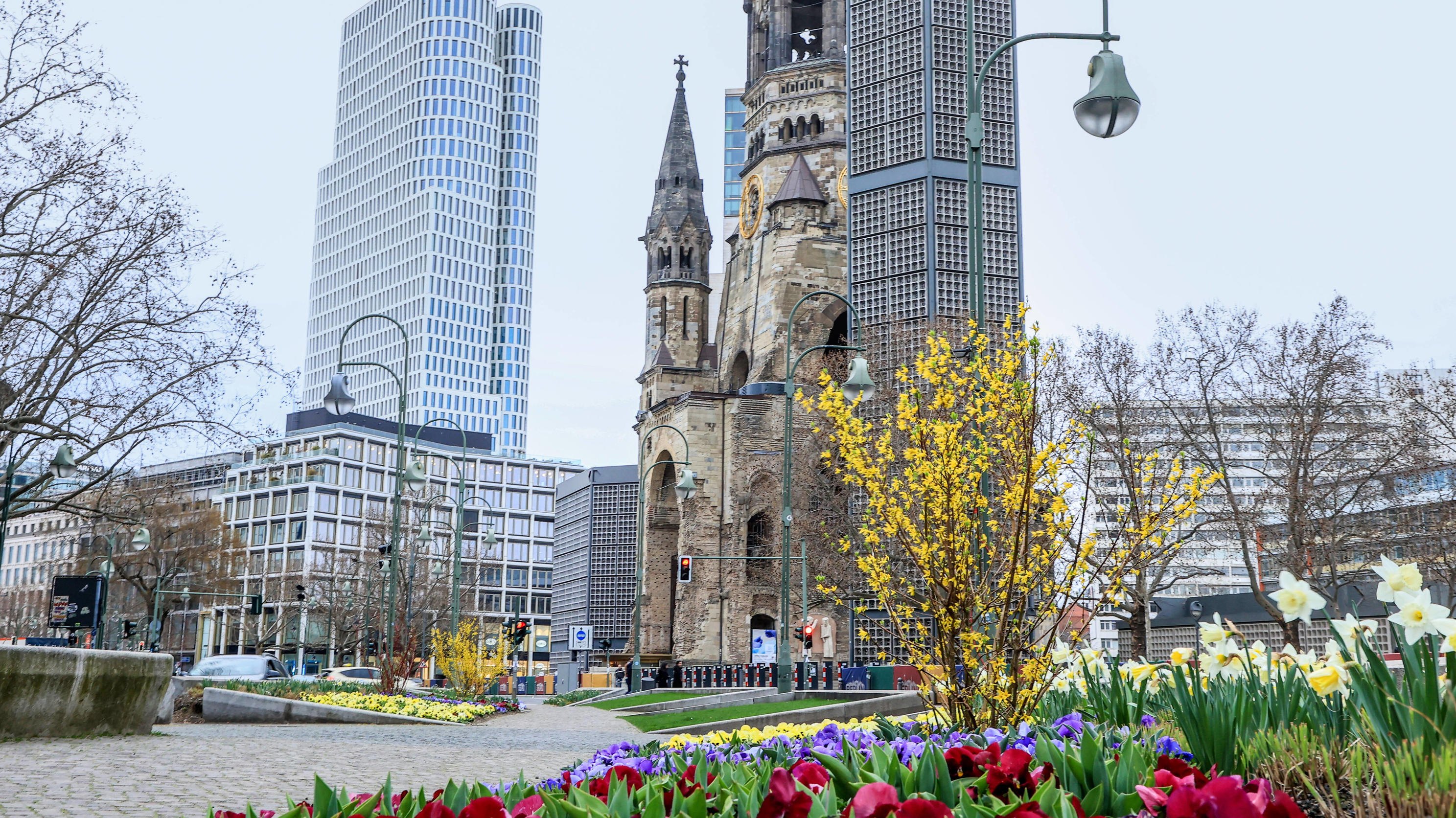 Berlin beschließt mehr Freiheiten für Geimpfte City Berlin Breitscheidplatz Berlin, 02.04.2021: Kaiser-Wilhelm-Gedaechtnis-Kirche neben Hotel Motel One Berlin-Upper West und Waldorf Astoria Berlin. Gelb bewachsenene Pflanzen, Tulpen und Veilchen in Osterzeit vor Gedaechtniskirche. Berlin Berlin