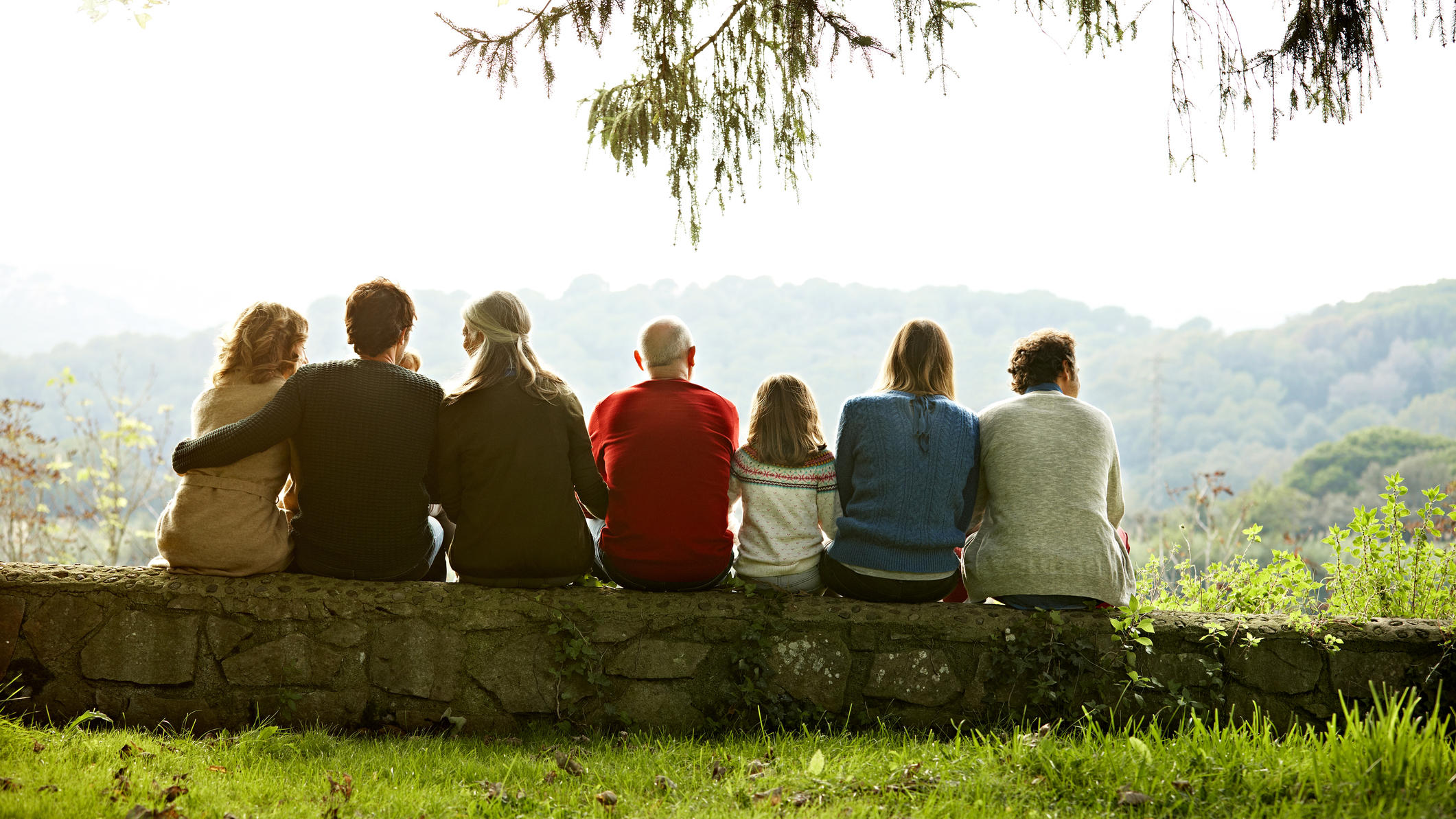 Wie ansteckend sind Geimpfte? Familie sitzt eng zusammen auf einer Mauer.