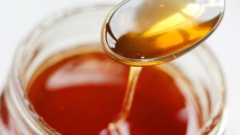 Top 5 - So retten Sie die Bienen! Honig fließt von einen Löffel zurück ins Honigglas.