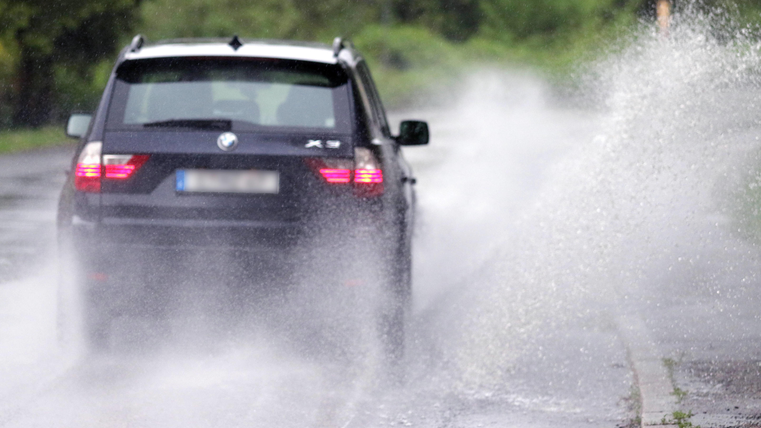 Warnungen vor Unwettern in Berlin, Sachsen, Thüringen, Sachsen-Anhalt, Brandenburg Gefährliche Straßenverhältnisse bei Starkregen. Das Wasser von einer nach Starkregen überfluteten Straße wird von den Autos in die Luft gerissen und sorgt bei vielen Fahrern für Schrecksekunden. Deutschland *** Dangerous ro
