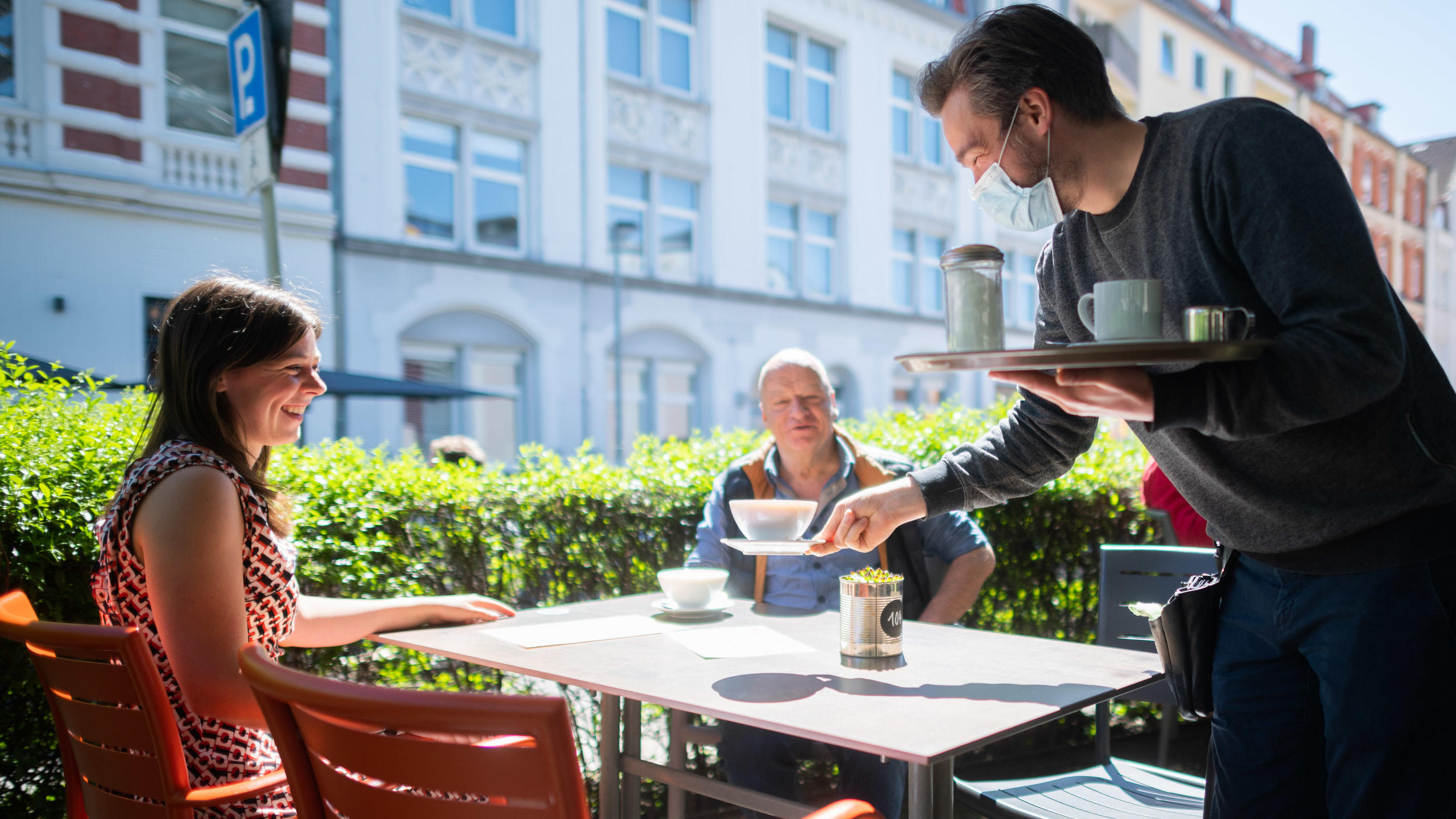 Niedersachsen führt 2G-Regel für weitere Bereiche ein 31.05.2021, Niedersachsen, Hannover: Kellner Alejandro serviert auf der Außenterrasse vom Café Mezzo an der Lister Meile Kaffee für die Gäste Mirella und Holger. In Niedersachsen wurde die Corona-Verordnung auch für die Gastronomie gelockert. Bei ent