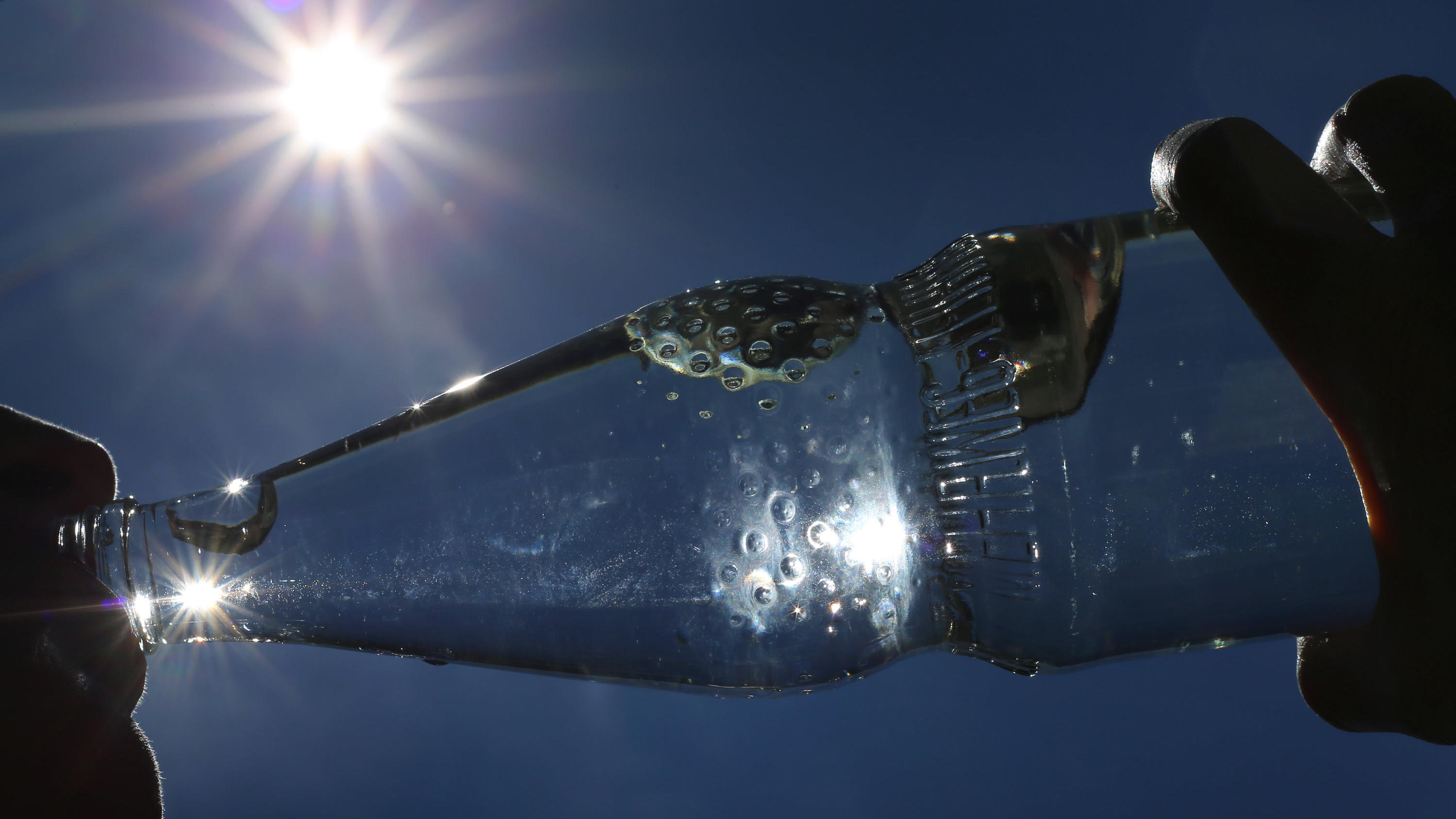 Was tun bei Hitze? Zehn Tipps für eine erfrischende Abkühlung Eine Frau trinkt im Sonnenschein aus einer Flasche sprudelndes Mineralwasser. Draußen ist es richtig heiß - ein kaltes Getränk muss her. Aber ist das eigentlich eine gute Idee? (zu dpa: