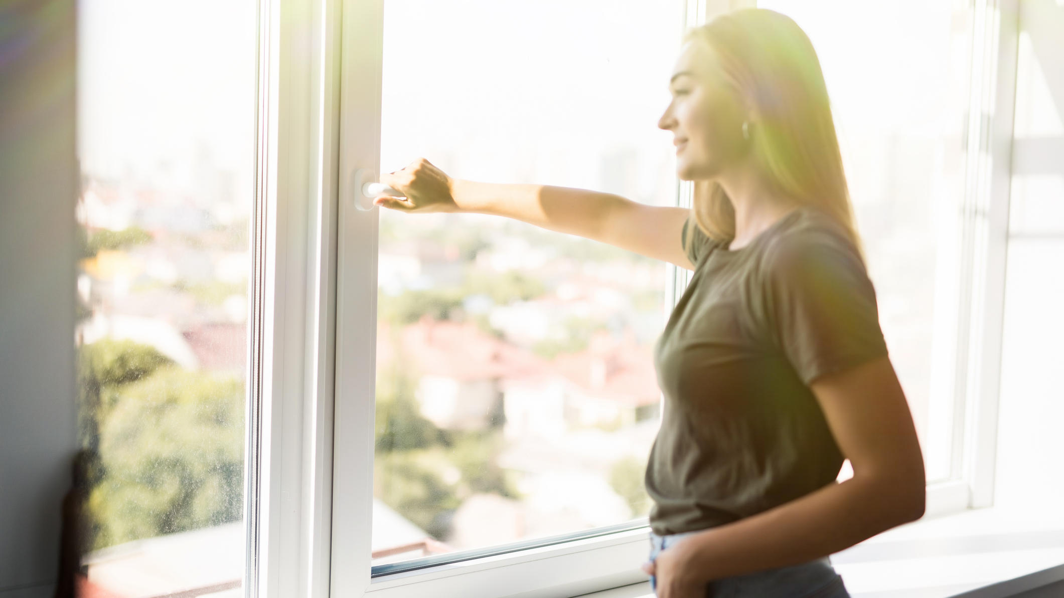 Fenster auf oder zu: Wie lüftet man bei großer Hitze richtig? Frau öffnet Fenster im Sommer