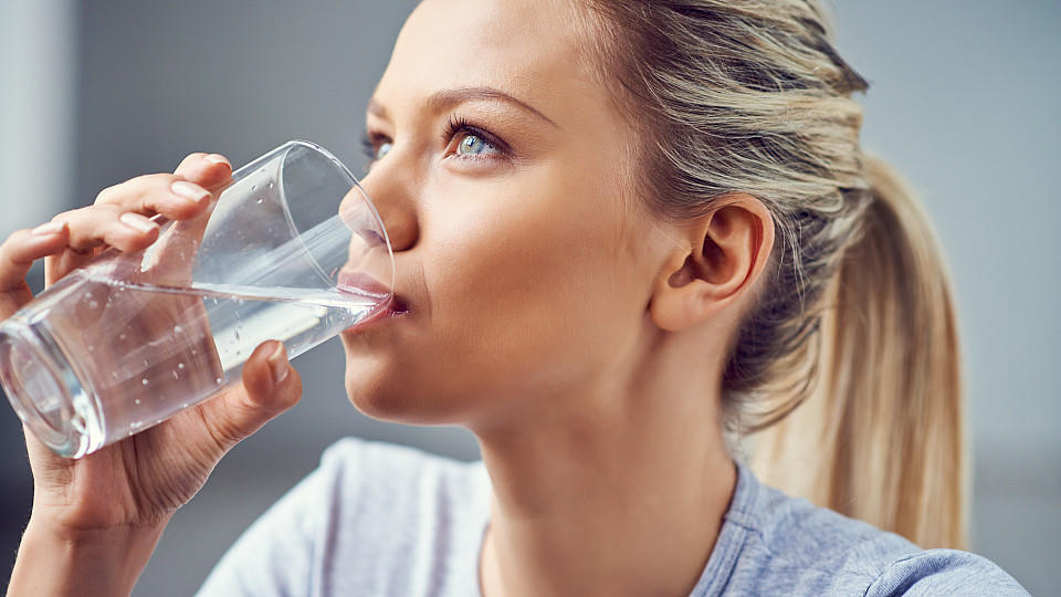 Hitze-Welle: Was wirklich bei Sonnenbrand hilft Eine junge Frau trinkt stilles Wasser aus einem Glas.