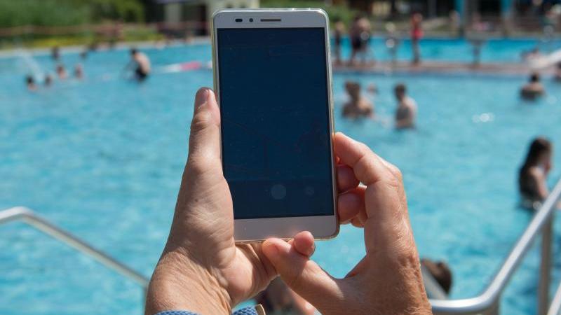 Schwimmbad-Betreiber warnt: Eltern lassen sich zu sehr vom Handy ablenken Eine Frau hält im Freibad ein Smartphone in Richtung des Pools