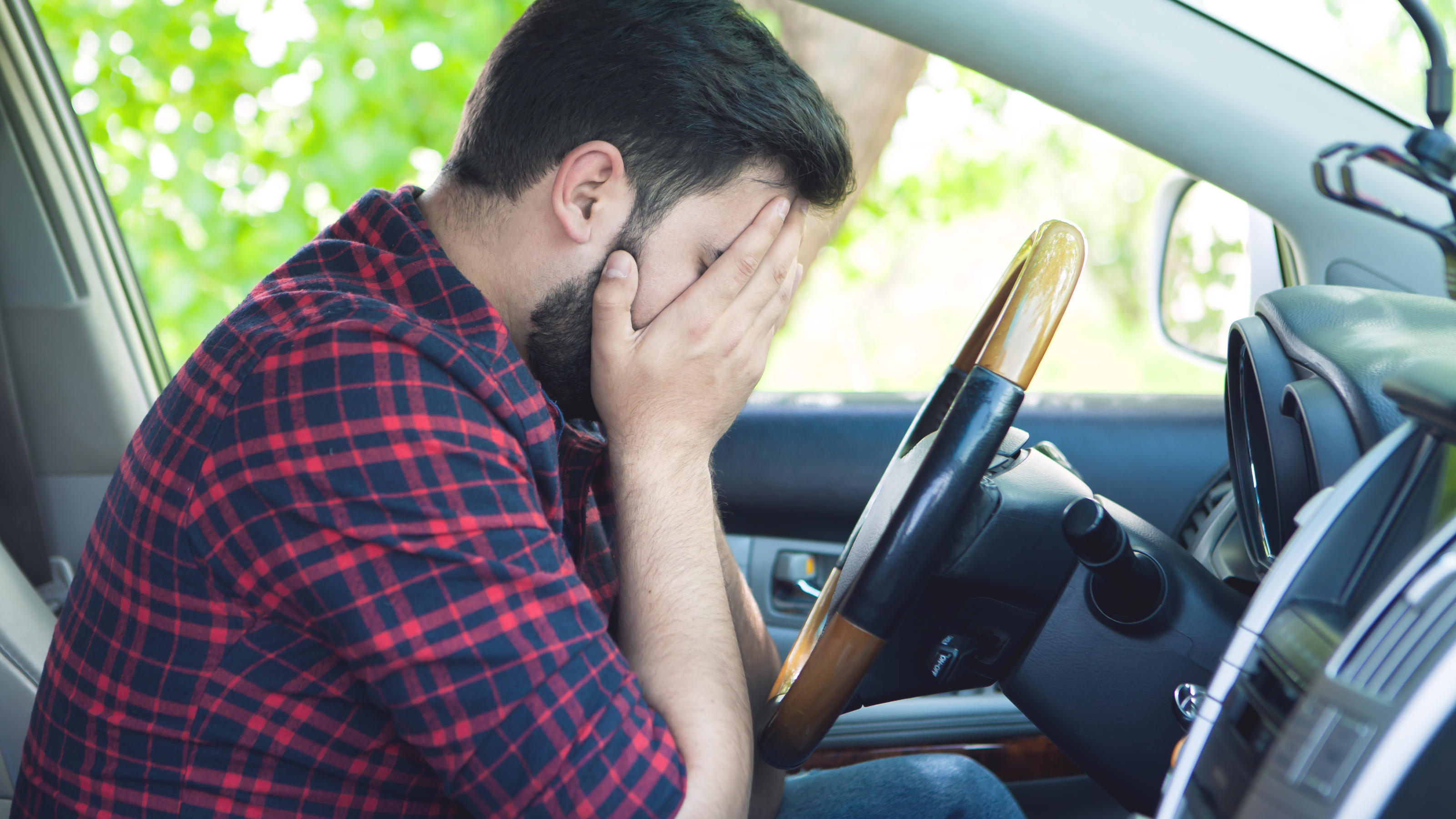 Amaxophobie: Wenn Autofahren zur Hölle wird Ein junger Mann sitzt verzweifelt am Steuer seines Autos. Er hat das Gesicht in seinen Händen vergraben.