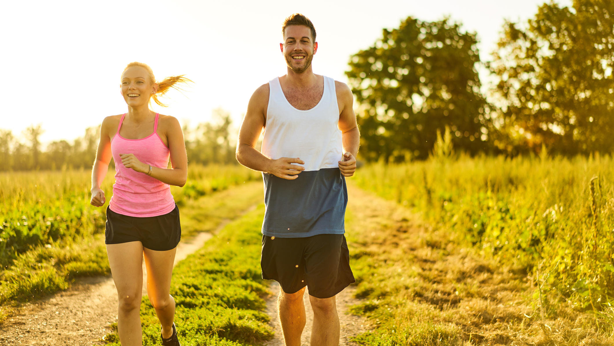 Amazfit-Fitness-Uhren im Test: Was bringen die Teile im Alltag? happy smiling young woman and man jogging on field path on sunny summer afternoon