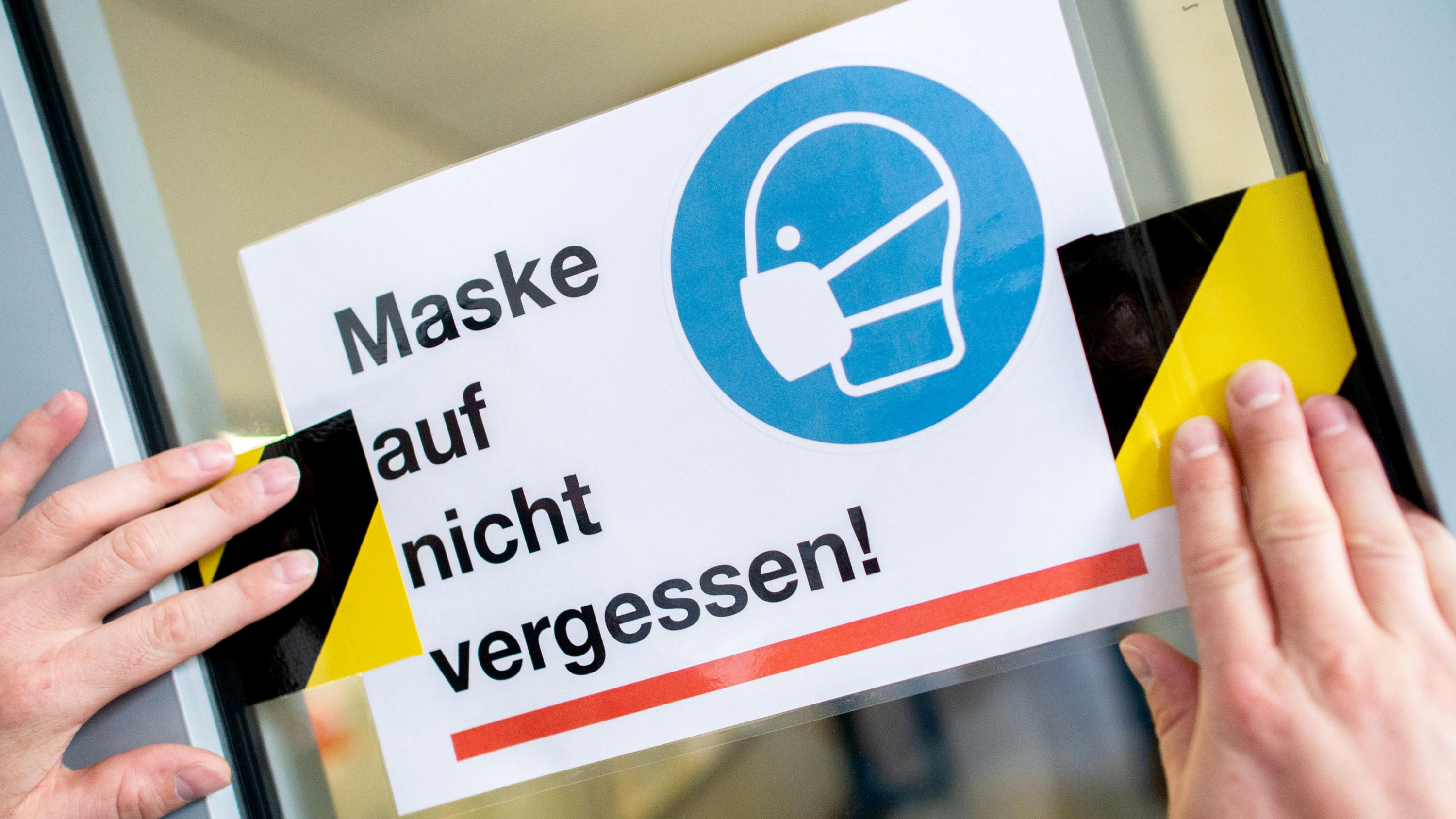 Corona-Auflagen: Das wollen SPD, Grüne und FDP ändern ARCHIV - 25.08.2020, Niedersachsen, Oldenburg: Der Hausmeister des Neuen Gymnasiums in Oldenburg klebt ein Schild mit der Aufschrift «Maske auf nicht vergessen!» an die Glasscheibe einer Zwischentür. (zu dpa: