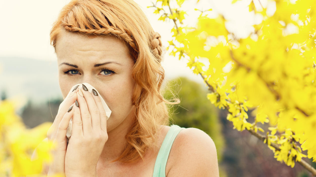 Pollenflug im Winter: Milde Temperaturen machen Allergikern das Leben schwer Young woman sneezing among flowers outdoors