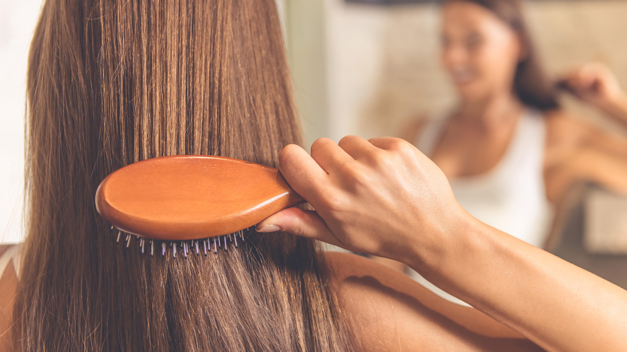 Diese 10 Probleme kennen alle Frauen mit langen Haaren Junge Frau kämmt vor dem Spiegel ihre langen Haare mit einer Bürste