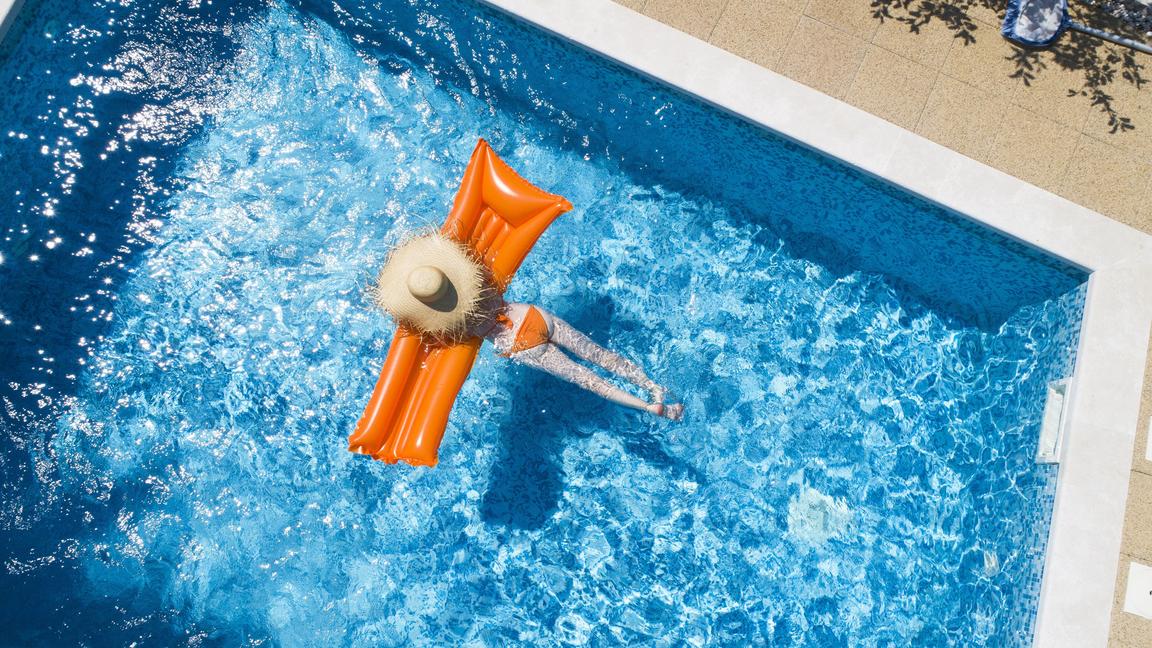 Back view of woman relaxing on orange airbed in swimming pool model released Symbolfoto property released PUBLICATIONxINxGERxSUIxAUTxHUNxONLY MAEF12347  