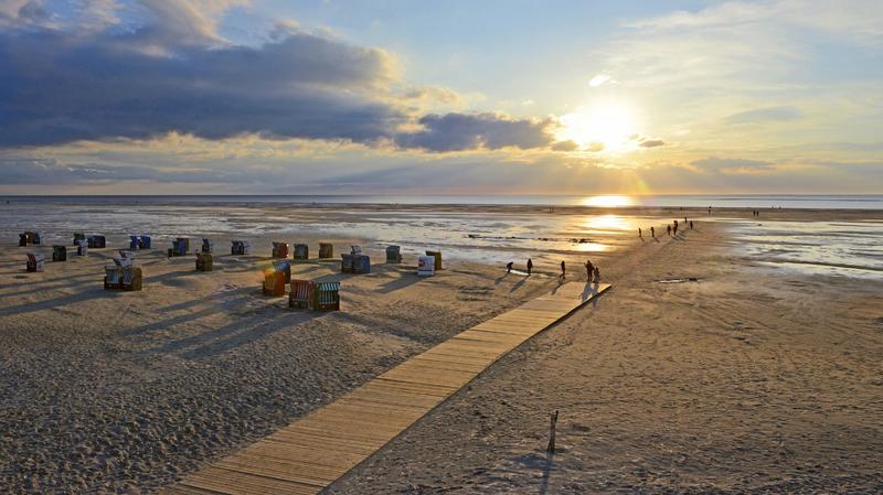Maritim: Urlauber als Schattenrisse vor der tiefstehenden Sonne am Strandübergang in Norddorf mit der Nordsee am Horizont