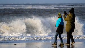 09.01.2019, Niedersachsen, Borkum: Eine Frau steht mit einem Kind am Strand vor den tosenden Wellen der Nordsee und macht ein Bild mit ihrem Handy. Foto: Mohssen Assanimoghaddam/dpa +++ dpa-Bildfunk +++