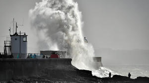 13.03.2019, Großbritannien, Porthcawl: Wellen brechen sich an der Hafenmauer, während Menschen das Schauspiel beobachten. Sturm Gareth hat in mehreren Teilen Großbritanniens zu Einschränkungen in Transport und Verkehr geführt und zieht jetzt nach Osten. Foto: Ben Birchall/PA Wire/dpa +++ dpa-Bildfunk +++