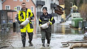 16.03.2019, Bayern, Passau: Feuerwehrleute tragen Sandsäcke und gehen auf einer Straße, die unter Wasser steht. Das Hochwasser der Ilz hat in Teilen Passaus Straßen und Grundstücke überflutet und Keller volllaufen lassen. Foto: Tobias Köhler/dpa +++ dpa-Bildfunk +++