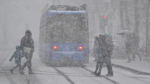 11.03.2019, Bayern, München: Passanten gehen bei Schneefall an einer Staßenbahn-Haltestelle über die Straße. Foto: Peter Kneffel/dpa +++ dpa-Bildfunk +++