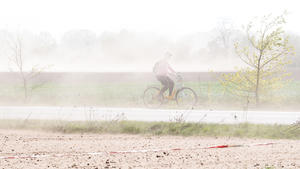 23.04.2019, Niedersachsen, Burgdorf: Eine Fahrradfahrerin fährt mit ihrem Rad über einen Fahrradweg, als starker Wind viel Sand von trockenen Feldern aufwirbelt. Foto: Julian Stratenschulte/dpa +++ dpa-Bildfunk +++