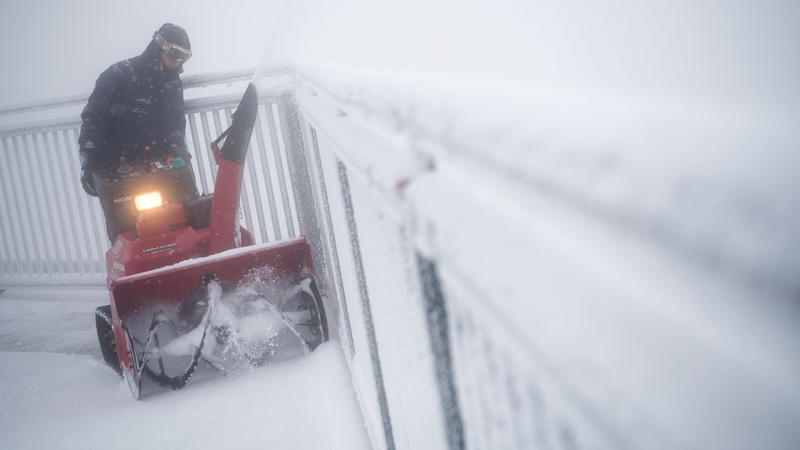 Bayern, Grainau: Ein Mann fährt mit einem Schneepflug auf dem Gipfel der Zugspitze über die Aussichtsplattform.