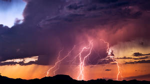Powerful lightning bolts strike from a sunset thunderstorm in the Arizona desert.