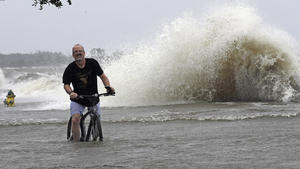 dpatopbilder - 13.07.2019, USA, Mandeville: Jeff Holland fährt mit dem Fahrrad durch Wasser, das durch Tropensturm «Barry» aus dem Lake Pontchartrain über den Damm geschoben wurde. Tropensturm «Barry» traf am Samstagnachmittag (Ortszeit) nahe der Stadt Intracoastal City westlich von New Orleans auf die Küste, wie das Nationale Hurrikan-Zentrum in Miami mitteilte. Foto: David J. Phillip/AP/dpa +++ dpa-Bildfunk +++