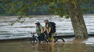 12.07.2019, USA, Philadelphia: Amy Norwitz und Jason Lubken schieben ihre Fahrräder über einen überfluteten Weg. Eine Reihe von Stürmen mit starken Regenfällen und Winden herrschte im Nordosten. Foto: Jessica Griffin/The Philadelphia Inquirer/AP/dpa +++ dpa-Bildfunk +++